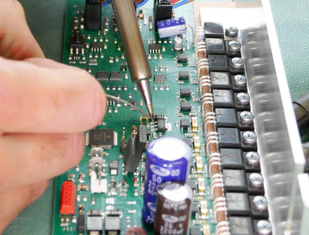 Eine Person lötet Komponenten auf eine grüne Leiterplatte, die mit verschiedenen elektronischen Bauteilen bestückt ist.