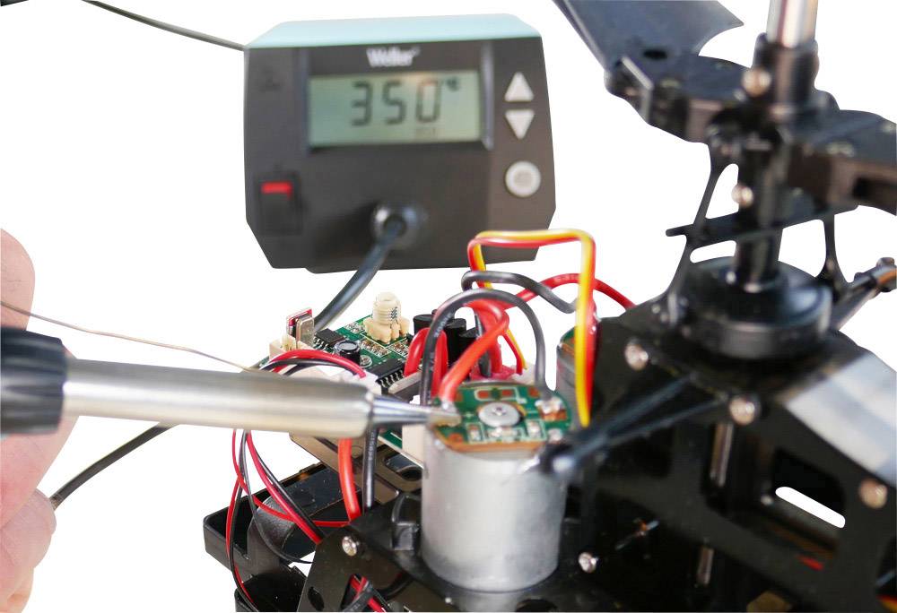 Lötkolben an einer Schaltung in einem technischen Aufbau, während ein Thermometer 350°C anzeigt; Fokus auf Präzision und Temperaturkontrolle.