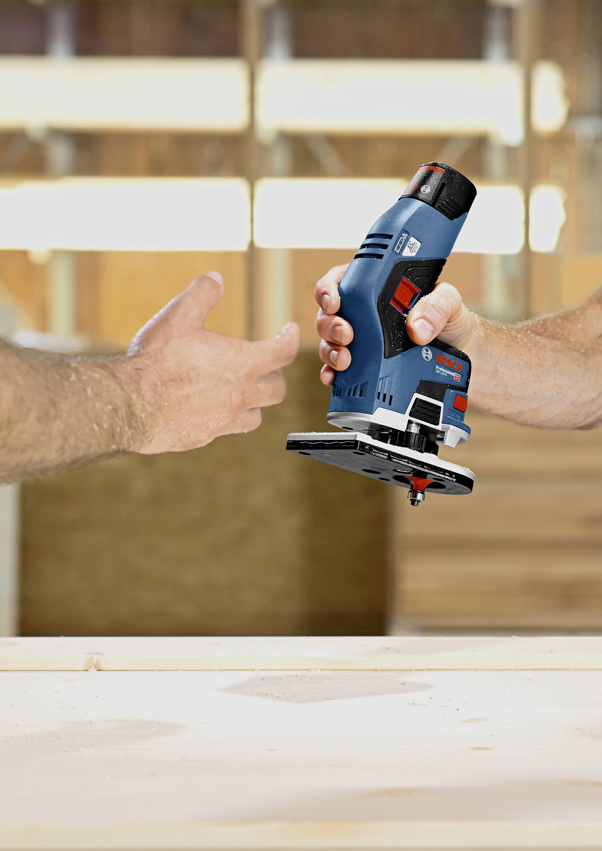 Eine Person übergibt einer anderen Person eine blaue elektrische Handfräse in einer Holzwerkstatt.