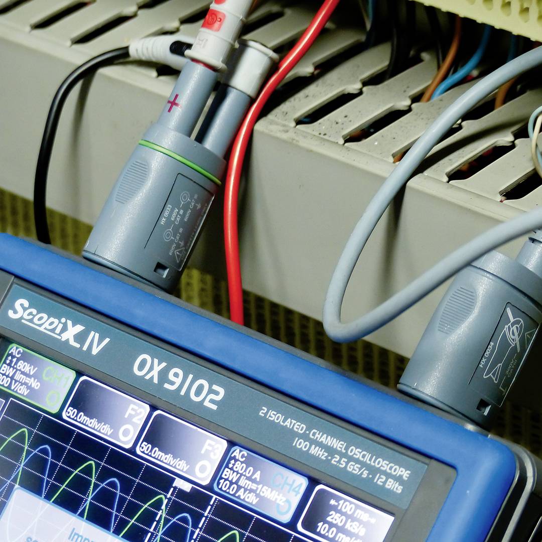 Ein Oszilloskop zeigt wellenförmige Signale auf einem Bildschirm. Messkabel sind angeschlossen, um Stromspannung zu messen.