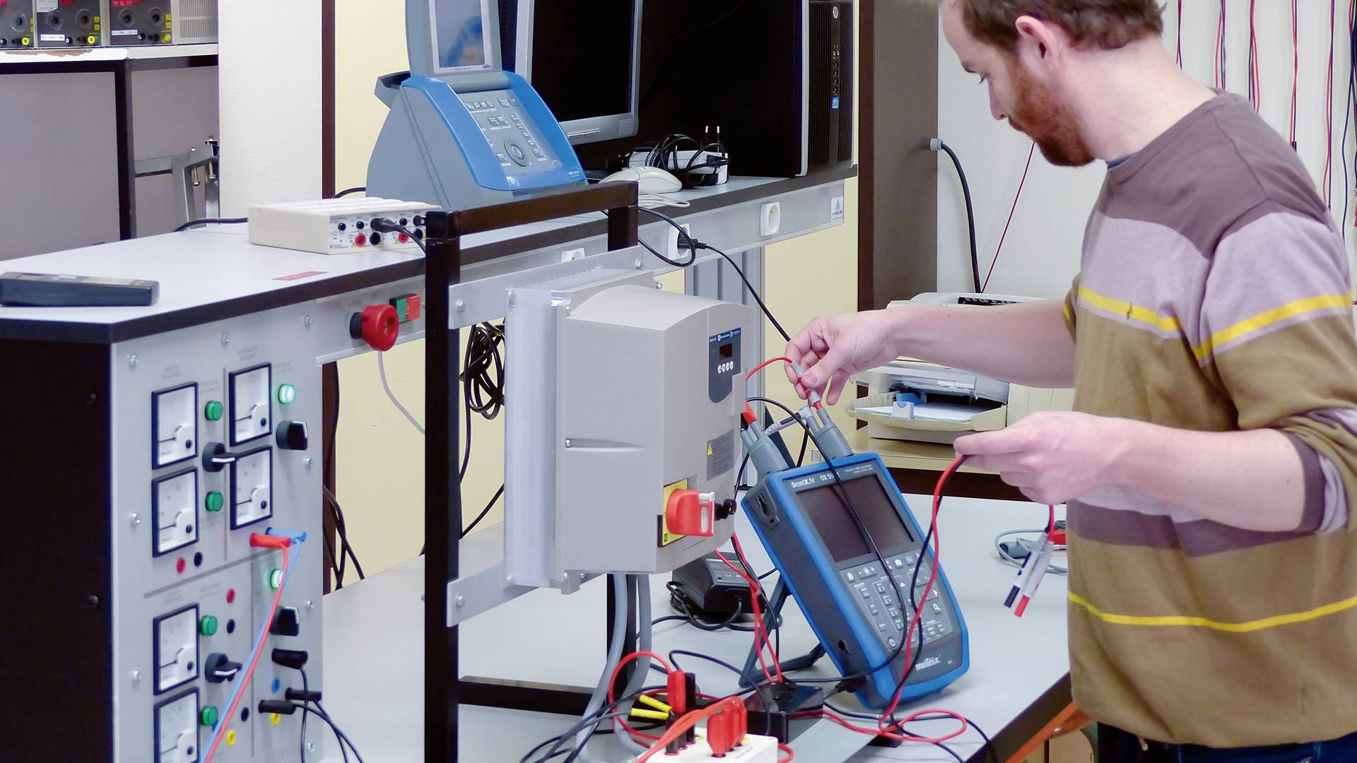 Ein Mann arbeitet an einem Testgerät in einem Labor. Auf dem Tisch befinden sich Messgeräte und elektronische Ausrüstung.