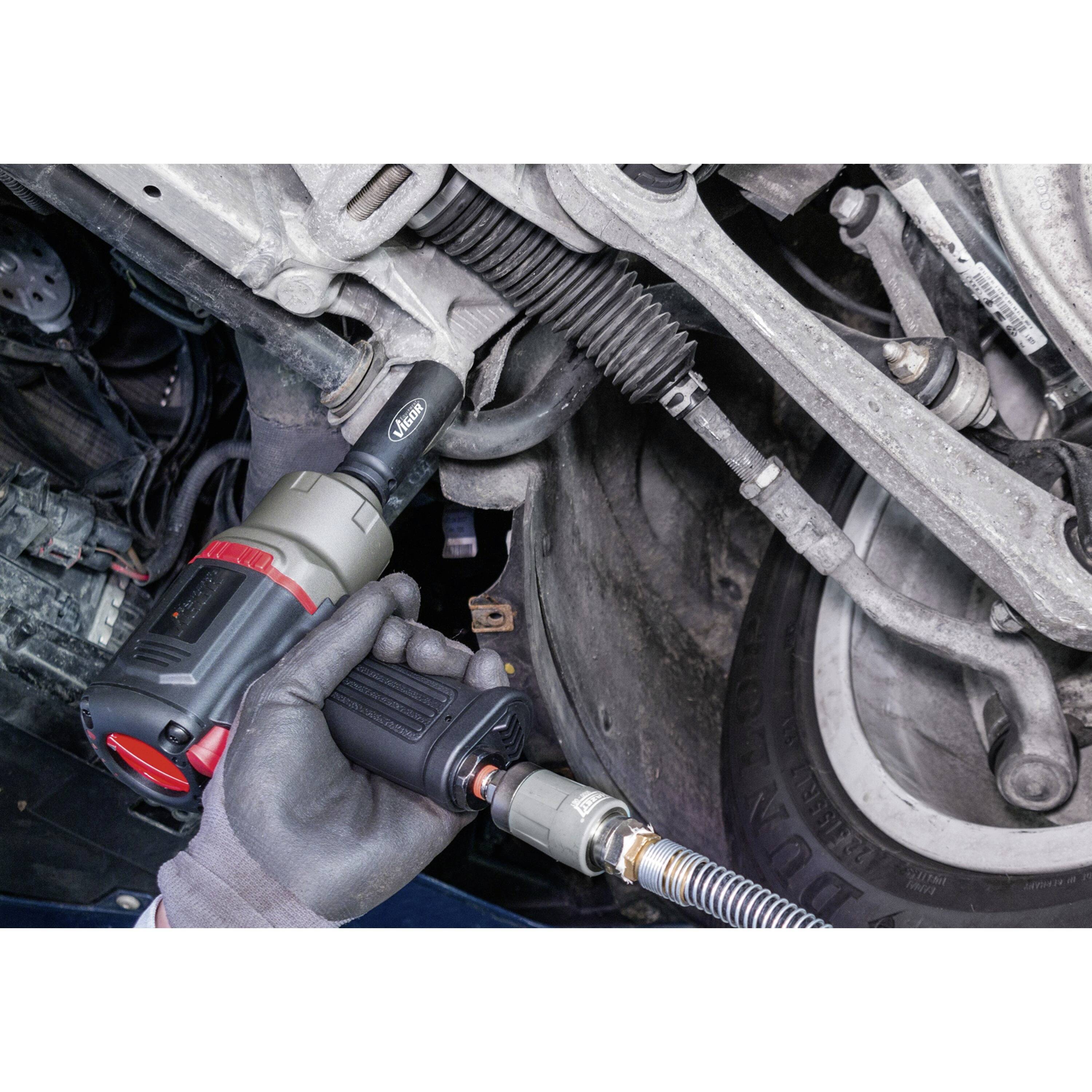 Ein Mechaniker verwendet eine Schlagschrauber, um ein Bolzen am Fahrzeug-Fahrwerk zu befestigen, mit dem Fokus auf dem Werkzeug im Einsatz unter dem Fahrzeug.