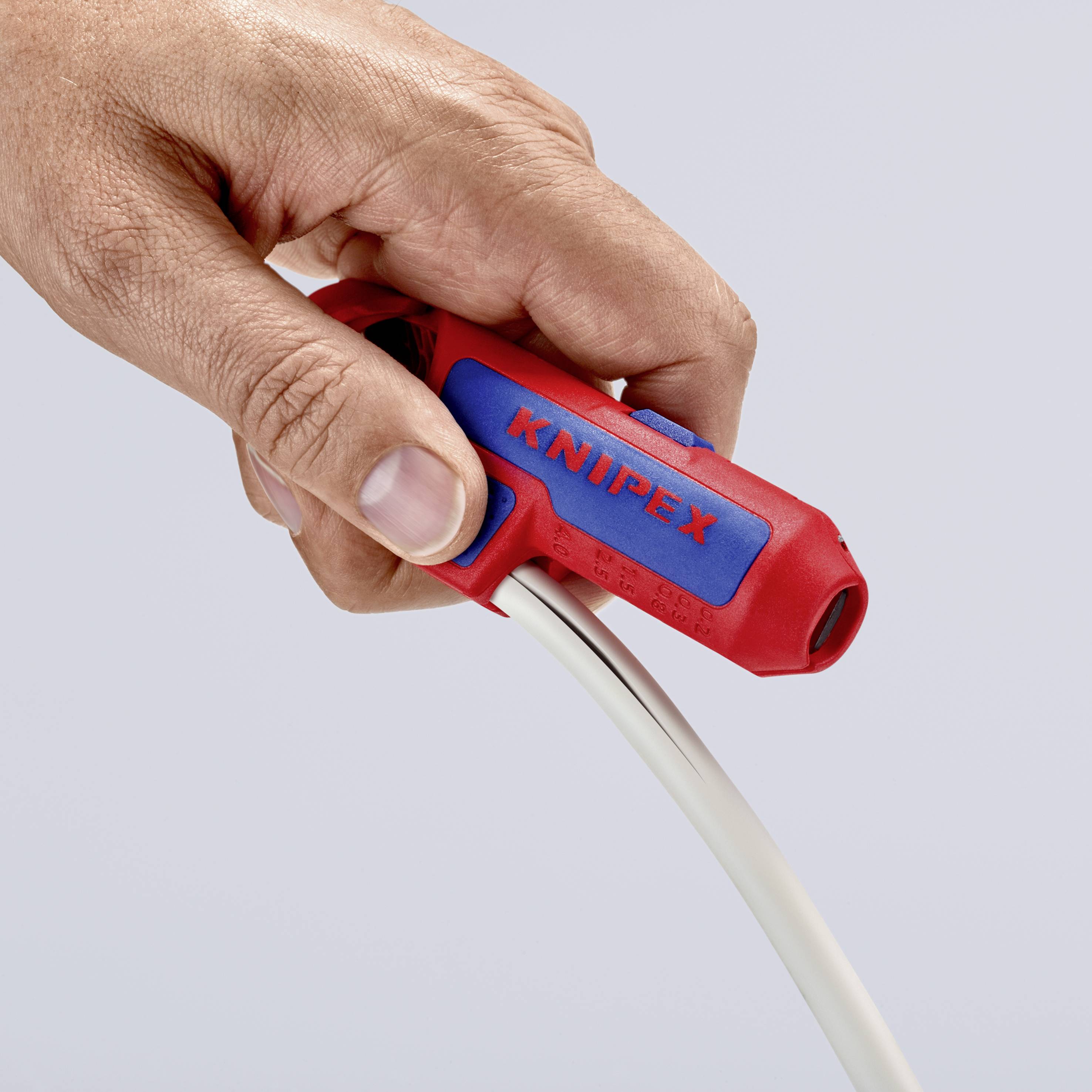 Eine Hand hält ein rotes Werkzeug der Marke Knipex, das zum Abisolieren eines weißen Kabels verwendet wird.