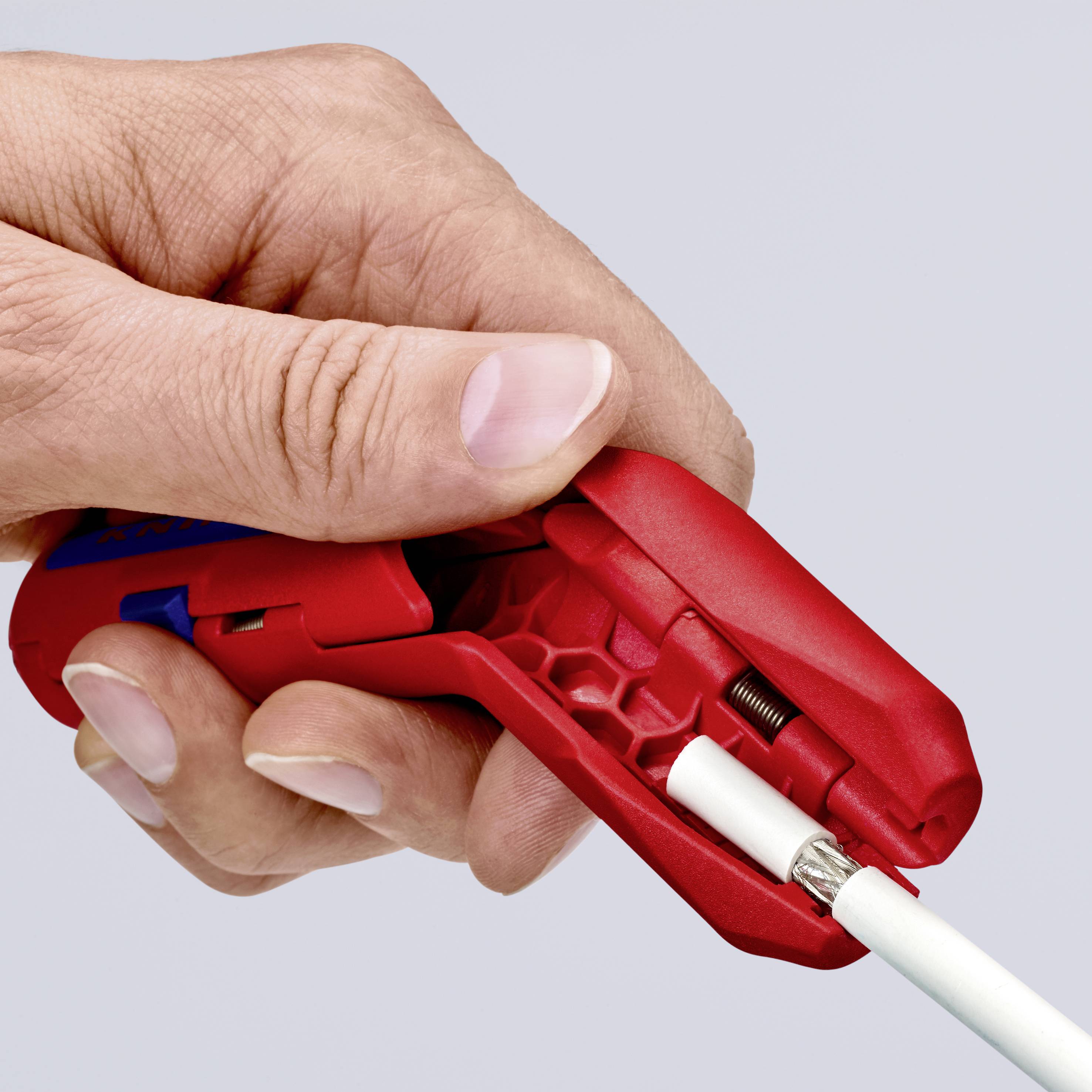 Eine Hand hält einen roten Drahtschneider, der ein Kabel abisoliert. Der Fokus liegt auf dem Werkzeug und dem präzisen Schneiden.