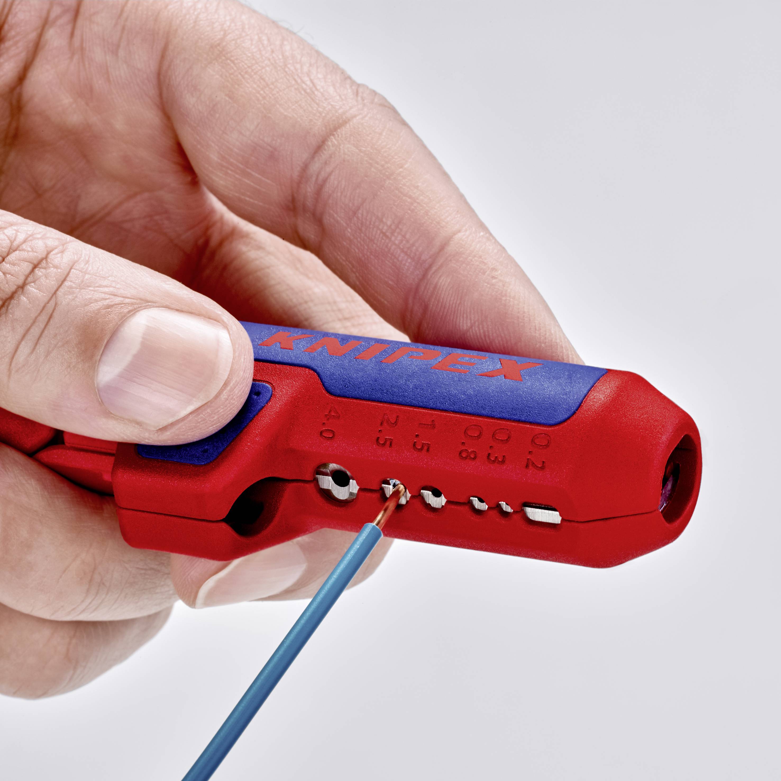 Eine Hand hält ein rot-blaues Abisolierwerkzeug der Marke Knipex, verwendet zum Abisolieren eines blauen Kabels.