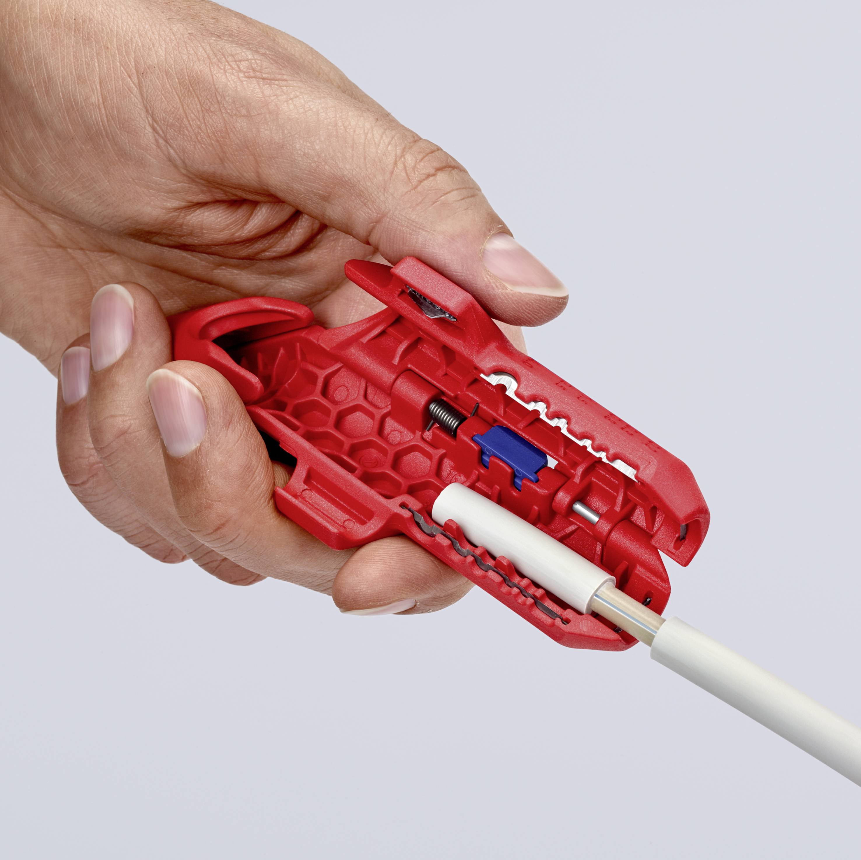 Hand hält rotes Kabelabisolierwerkzeug mit einem weißen Kabel darin.