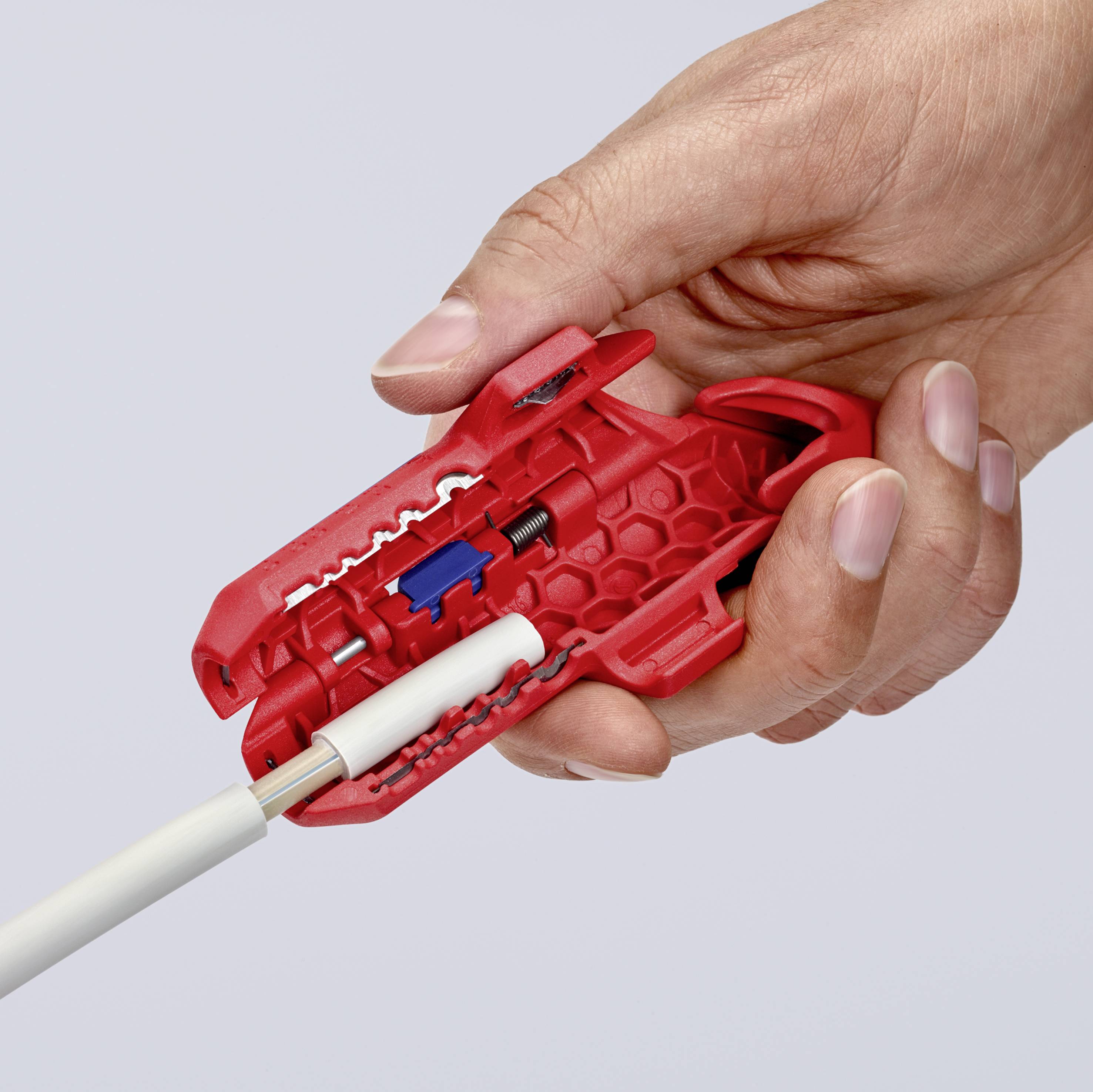 Eine Hand hält ein rotes Werkzeug zum Abisolieren von Kabeln, während ein weißes Kabel durch das Werkzeug gezogen wird.