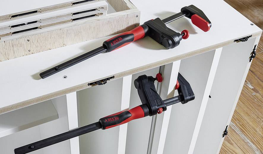 Zwei rote und schwarze Schraubzwingen fixieren ein Möbelstück in der Werkstatt.