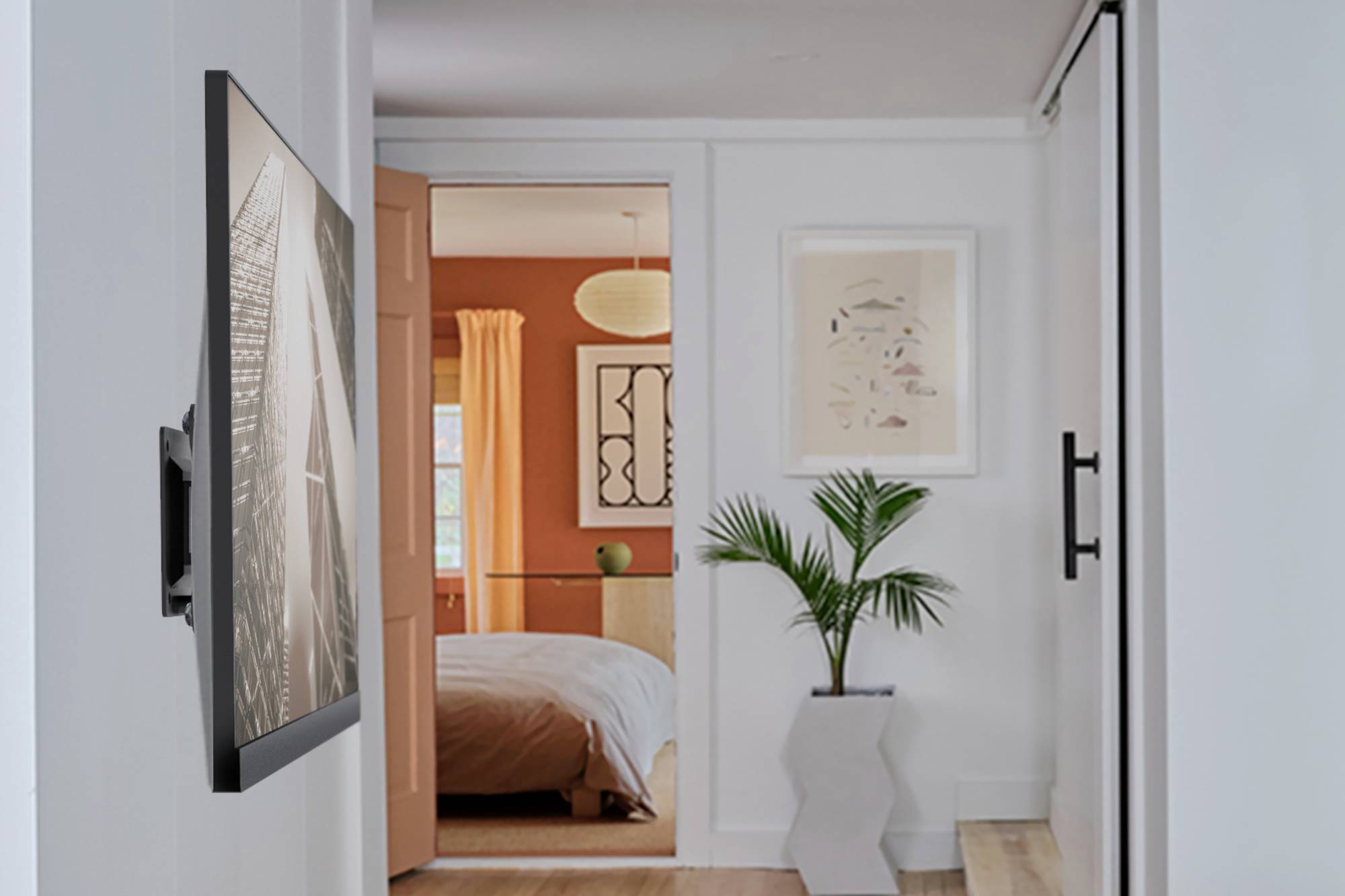 Ein moderner Flur mit eingelassenem Wandbild führt in ein Schlafzimmer mit orangefarbenen Wänden und weißen Möbeln. Eine Palme steht davor.