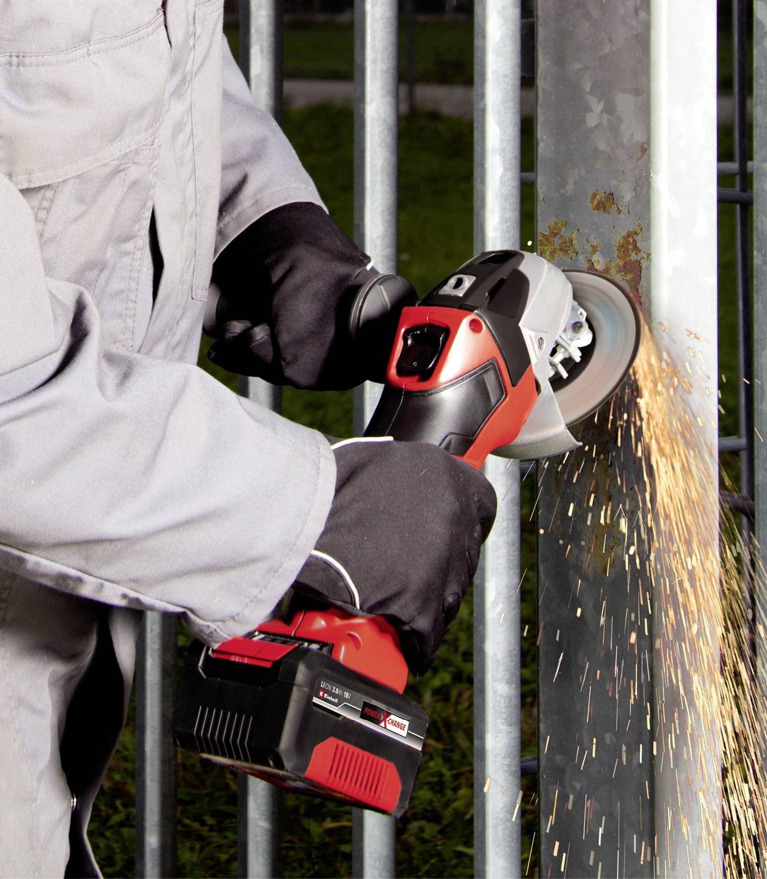 Eine Person schleift mit einem roten Winkelschleifer Metall, Funken fliegen. Die Person trägt Schutzkleidung und Handschuhe.