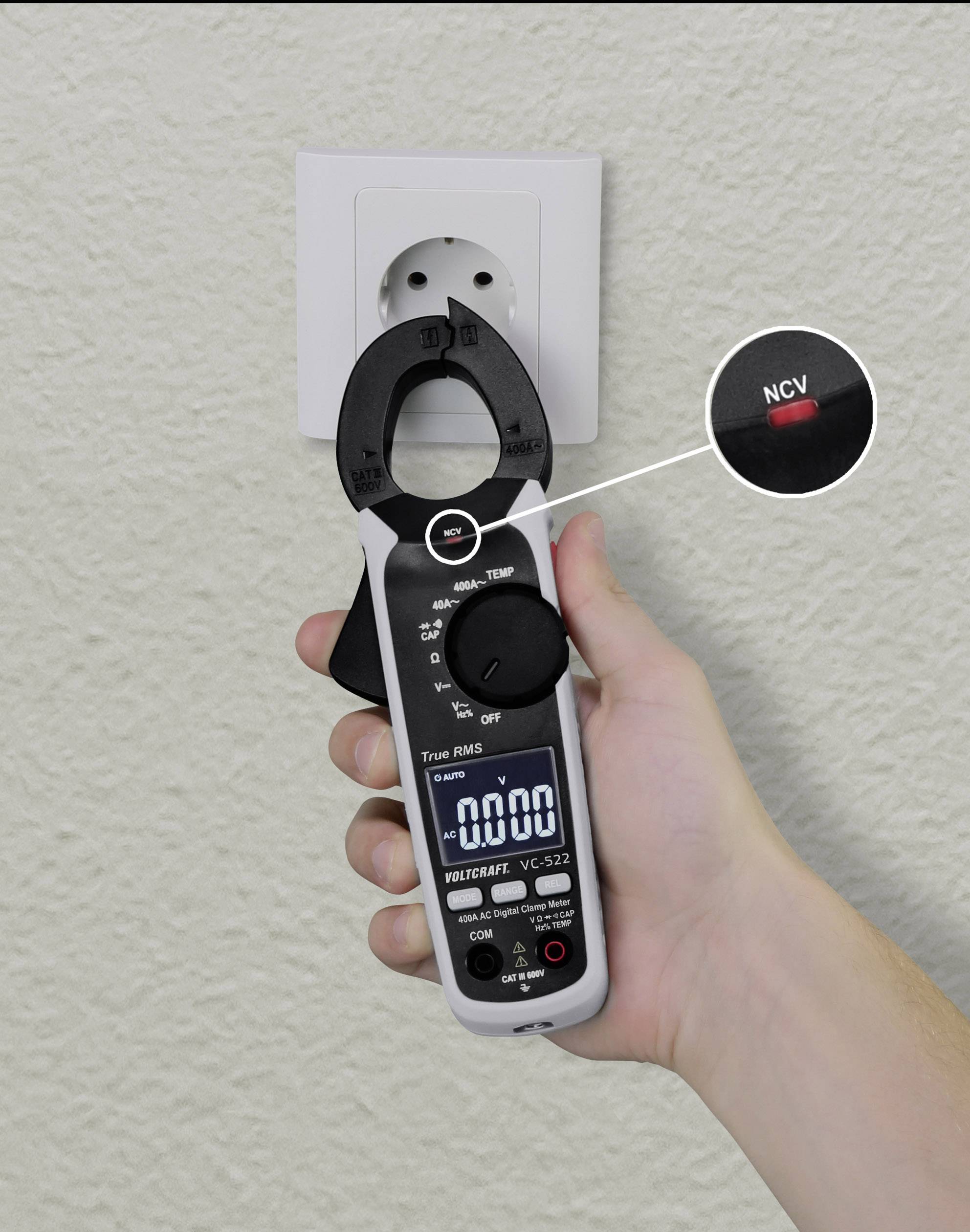 Multimeter wird an Steckdose gehalten, zeigt 0,00 Volt. Nahansicht des NCV-Knopfes. Wandsteckdose im Hintergrund.