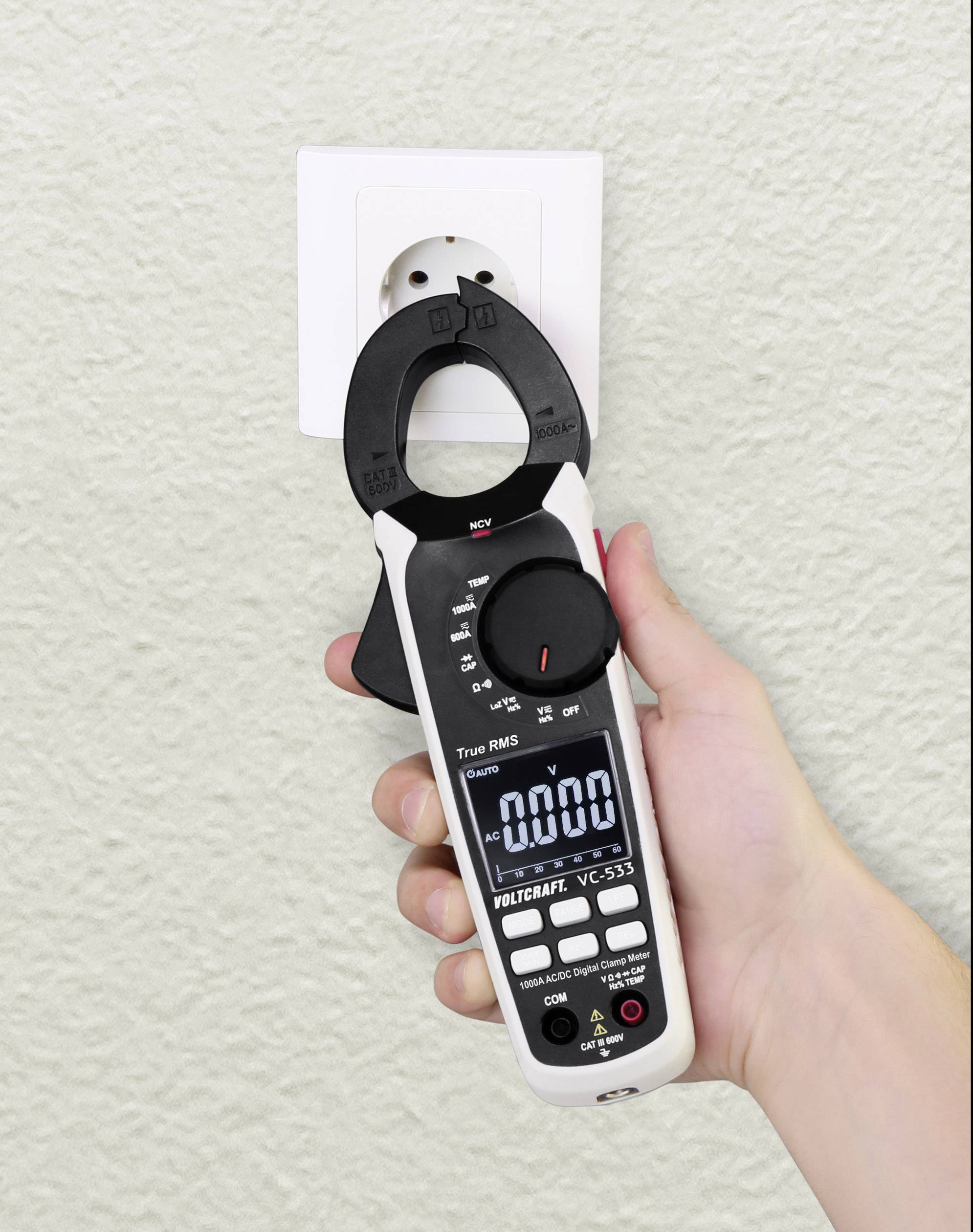 Eine Hand hält ein Multimeter vor einer Steckdose, zeigt 0.00 auf dem Display. Das Gerät wird möglicherweise auf Spannung geprüft.