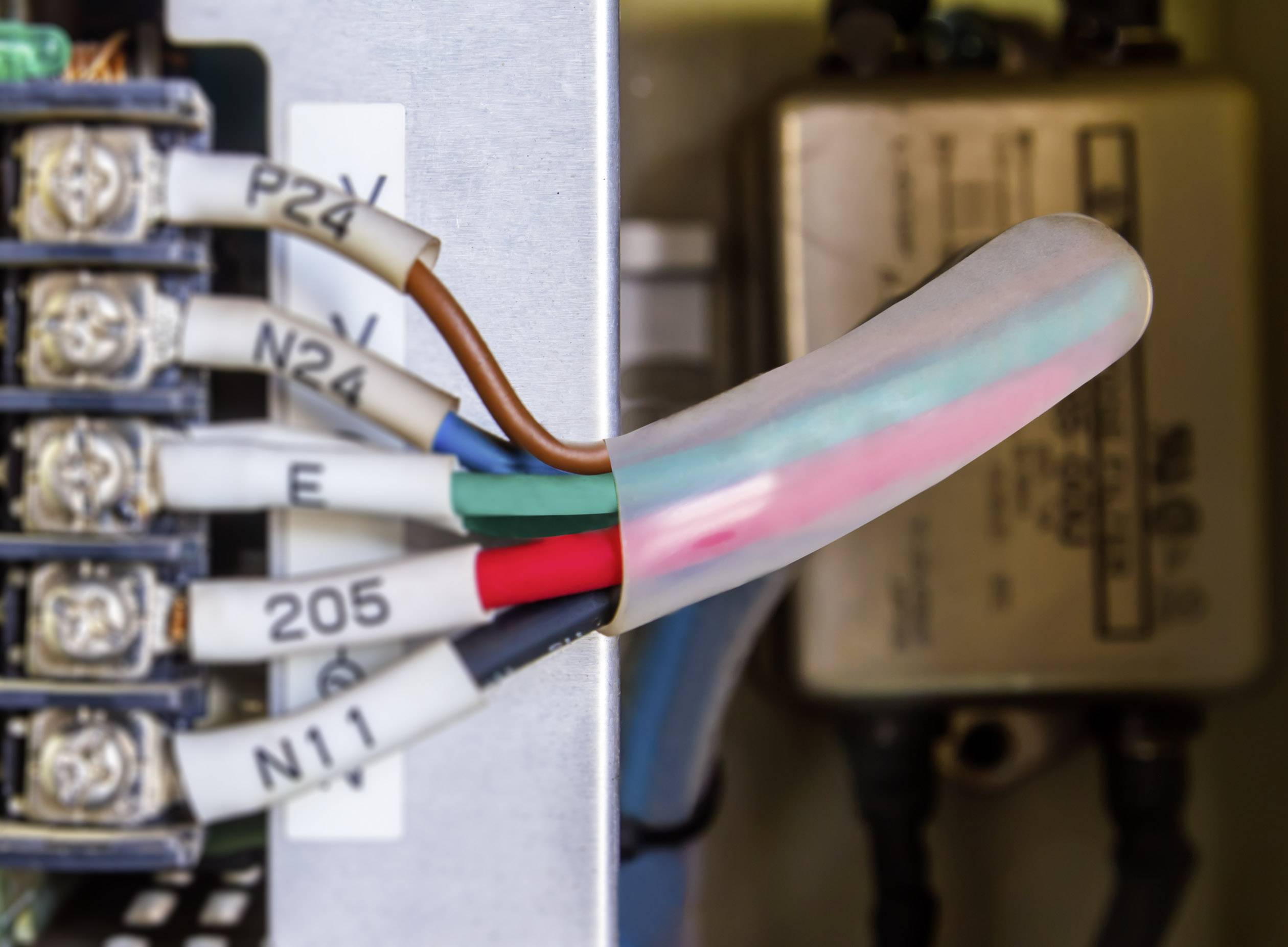 Wartungsfachkraft arbeitet an einem Schaltschrank mit verschiedenen Kabeln und Anschlüssen; Fokus auf bunte Kabelverbindungen.