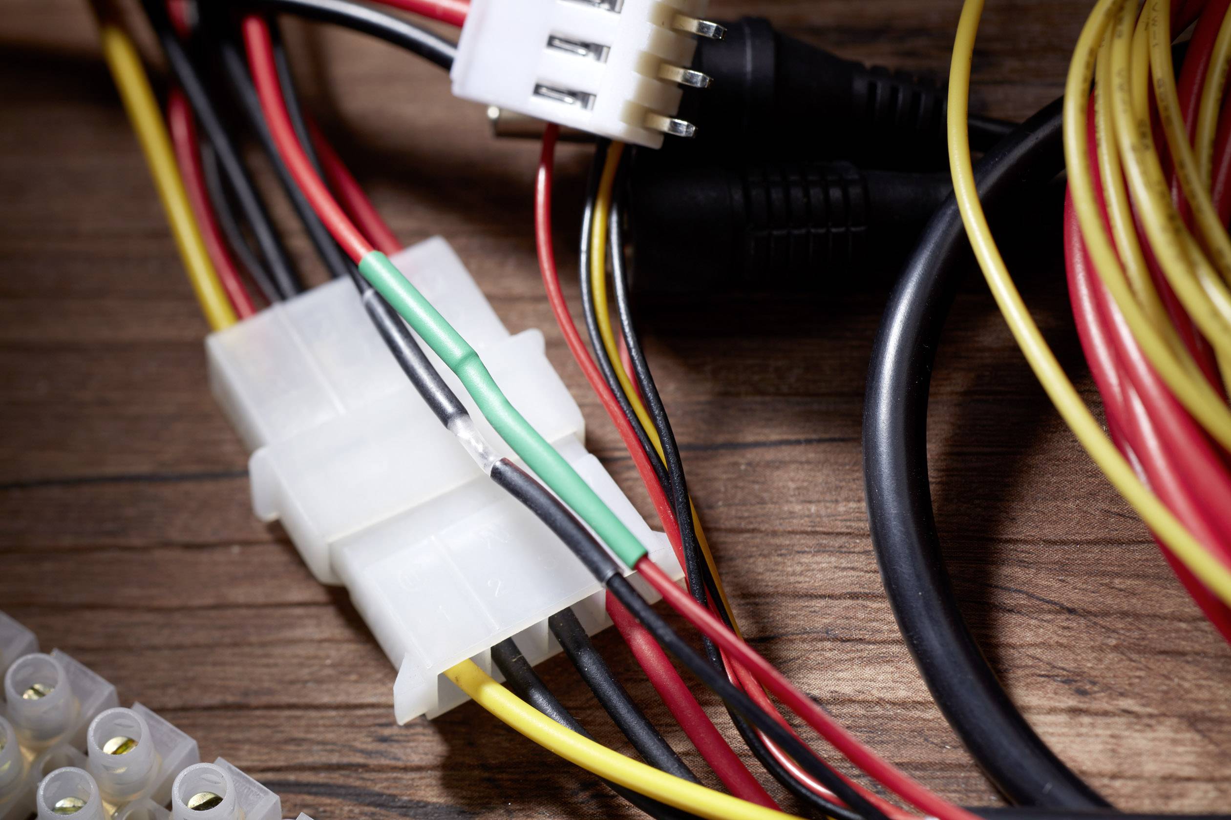 Mehrfarbige Kabel, die an einem weißen Stecker befestigt sind, liegen auf einer Holzoberfläche. Elektronisches Zubehör.