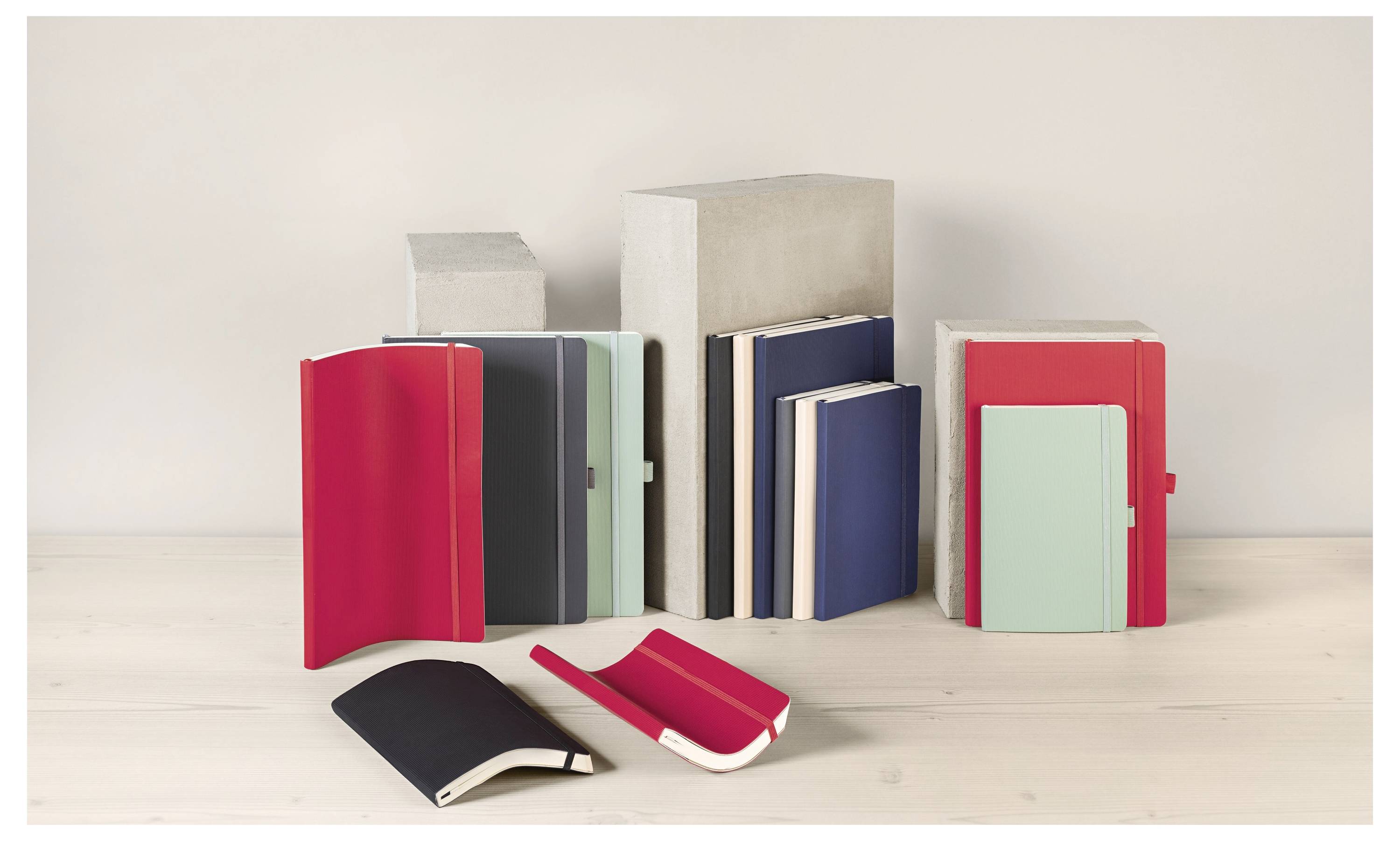 Sammlung farbenfroher Notizbücher und Hefte, die auf einem hellen Regal angeordnet sind, wobei mehrere aufrecht stehen und zwei offen davor liegen.