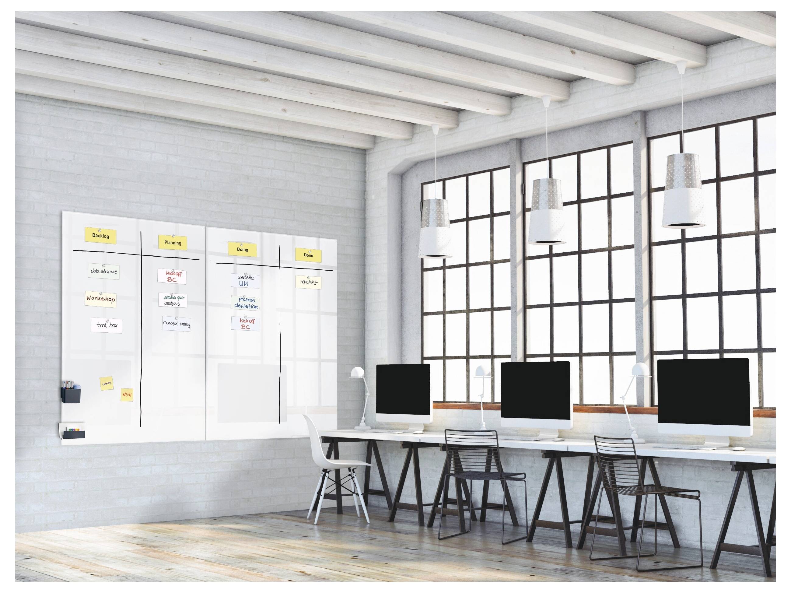 Moderner Büroarbeitsplatz mit einer Wandplanungstafel, drei Desktop-Computern, Stühlen und großen Fenstern, die natürliches Licht hereinlassen.