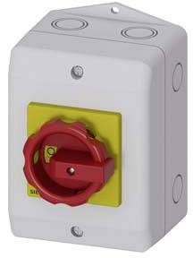 Ein grauer elektrischer Sicherheitsschalter mit rotem Drehgriff und gelbem Hintergrund, an einer Wand montiert.