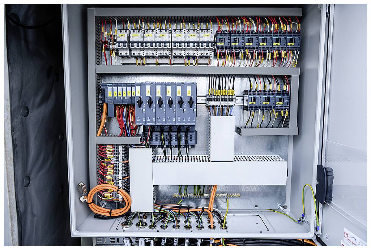 Ein geöffneter Schaltschrank zeigt diverse elektrische Komponenten und farbige Kabel.
