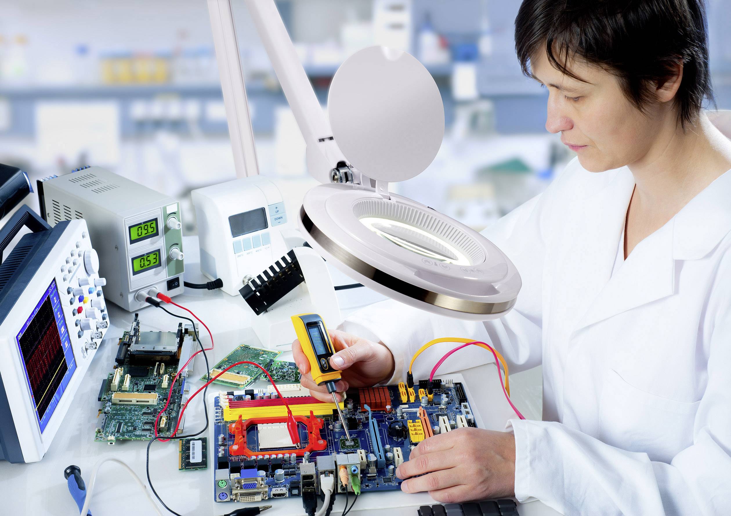 Eine Person in einem Labor arbeitet an elektronischen Bauteilen auf einer Leiterplatte, umgeben von Messgeräten und einem Vergrößerungsglas.