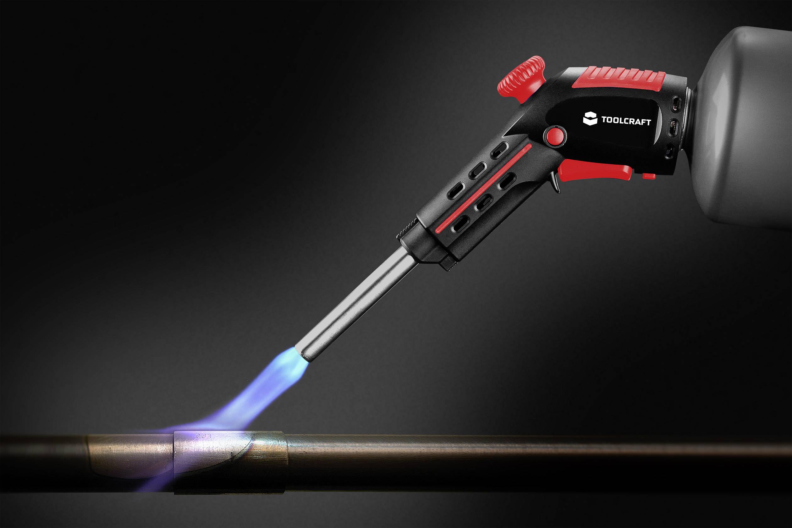 Lötbrenner von Toolcraft erhitzt ein Metallrohr mit blauem Flammenstrahl, dunkler Hintergrund.