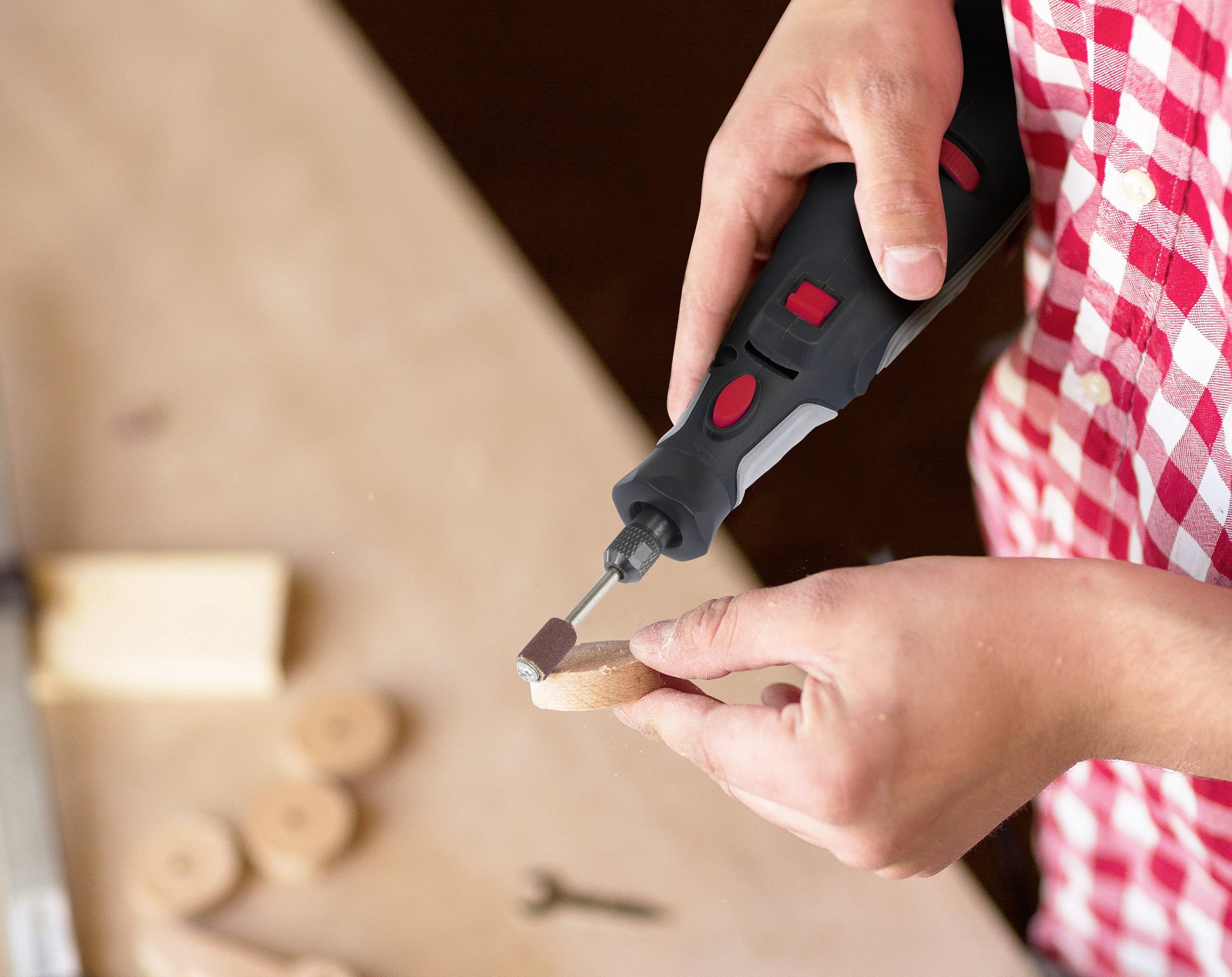 Eine Person bearbeitet ein rundes Holzstück mit einem rot-schwarzen elektrischen Schleifwerkzeug auf einem Tisch.