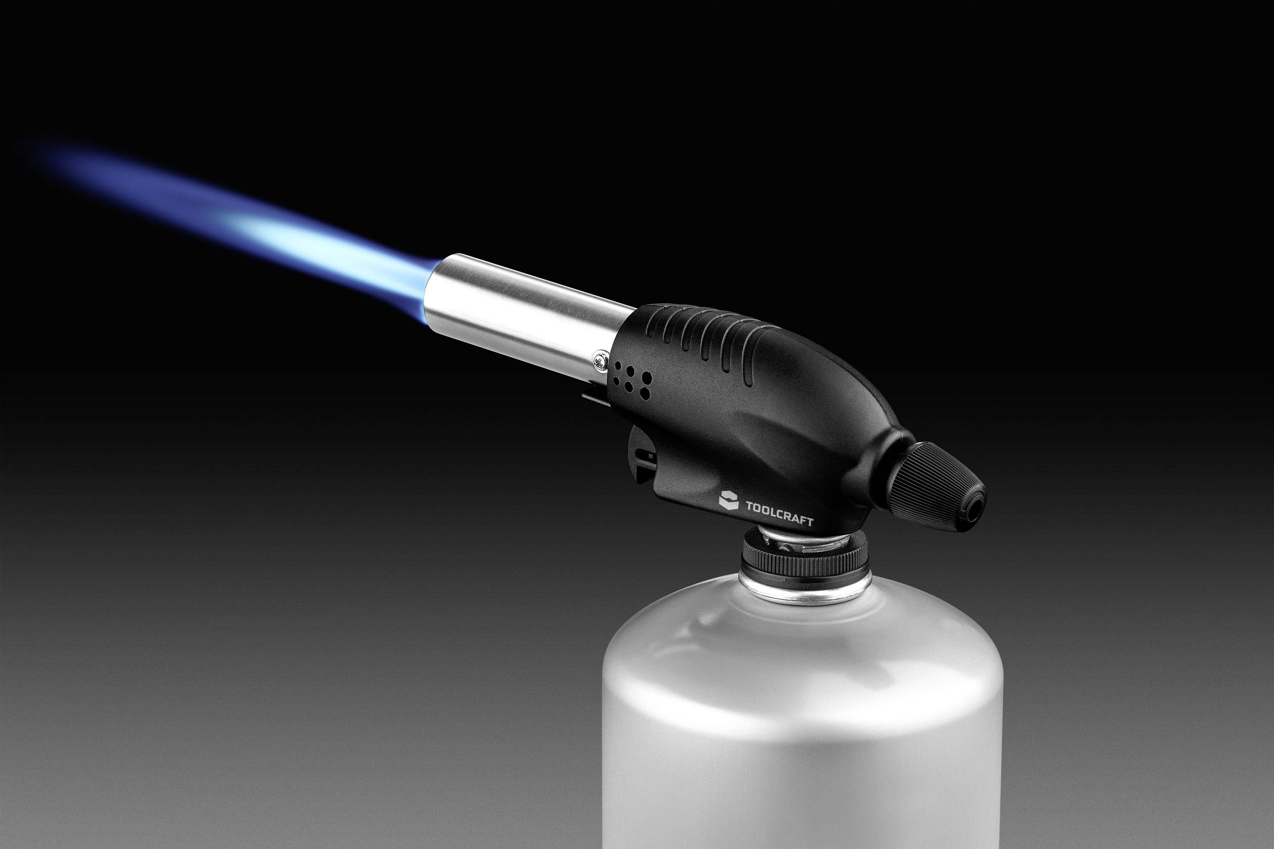 Ein Gasbrenner mit blauer Flamme, montiert auf einem silbernen Kanister, vor schwarzem Hintergrund.