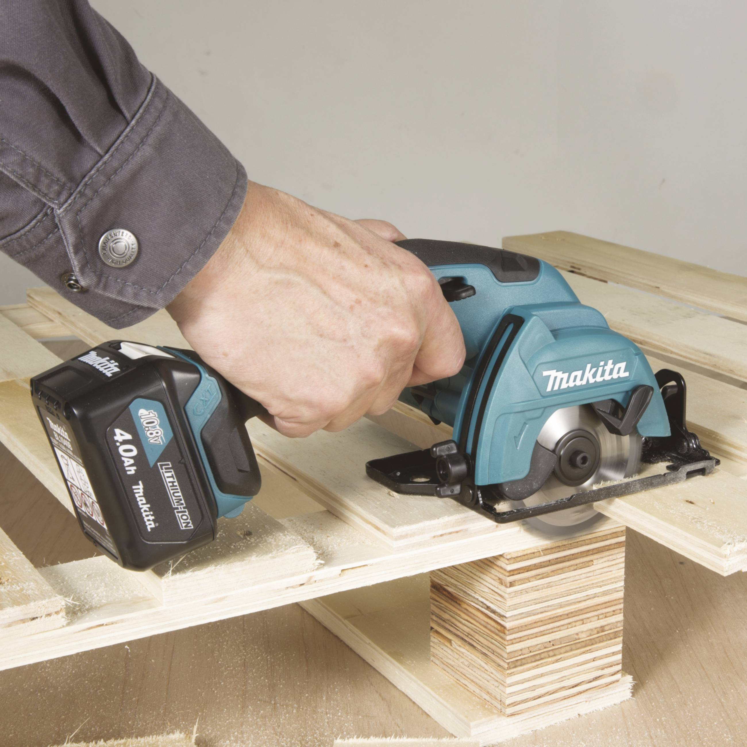 Eine Hand führt eine Akku-Kreissäge von Makita über ein Stück Holz. Die Säge schneidet gerade durch das Brett.