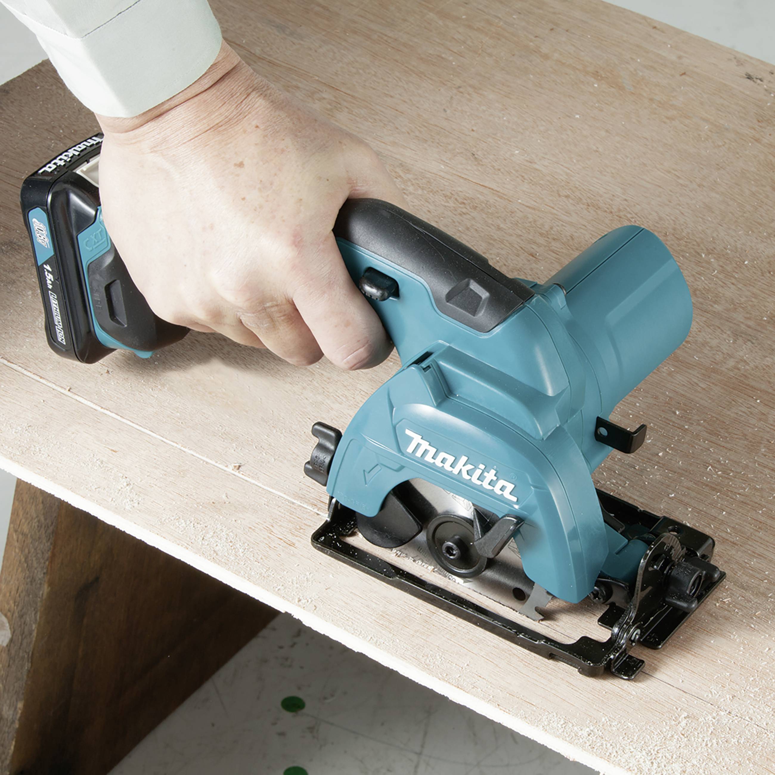 Eine Person hält eine blaue Handkreissäge und schneidet damit ein Holzbrett.