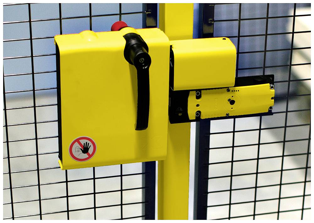 Gelbes Sicherheitsgerät an einem Metallgitter mit einem roten Not-Aus-Knopf und einem Warnaufkleber mit durchgestrichener Hand.