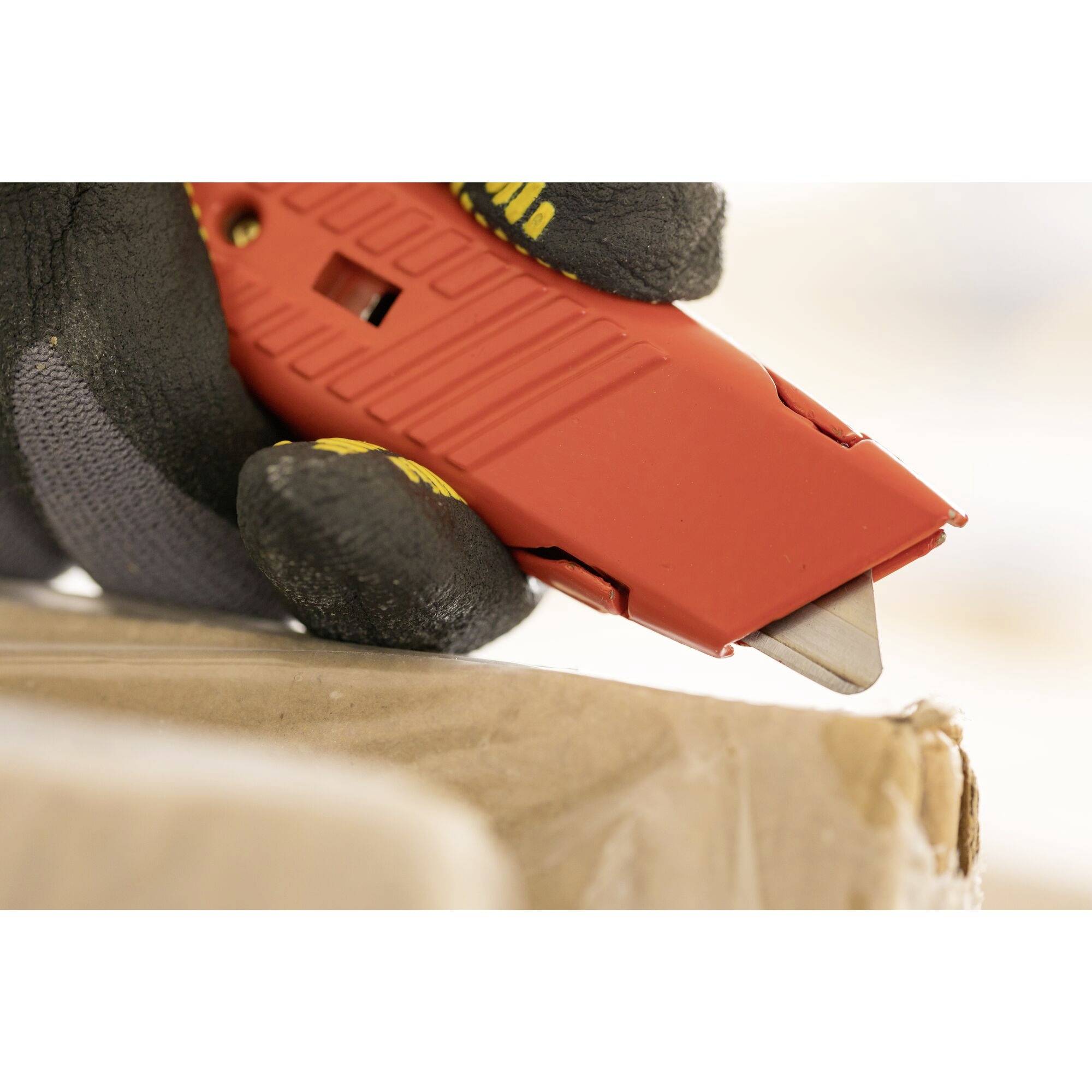 Hand in schwarzem Handschuh benutzt ein rotes Schneidewerkzeug, um einen Karton zu öffnen.