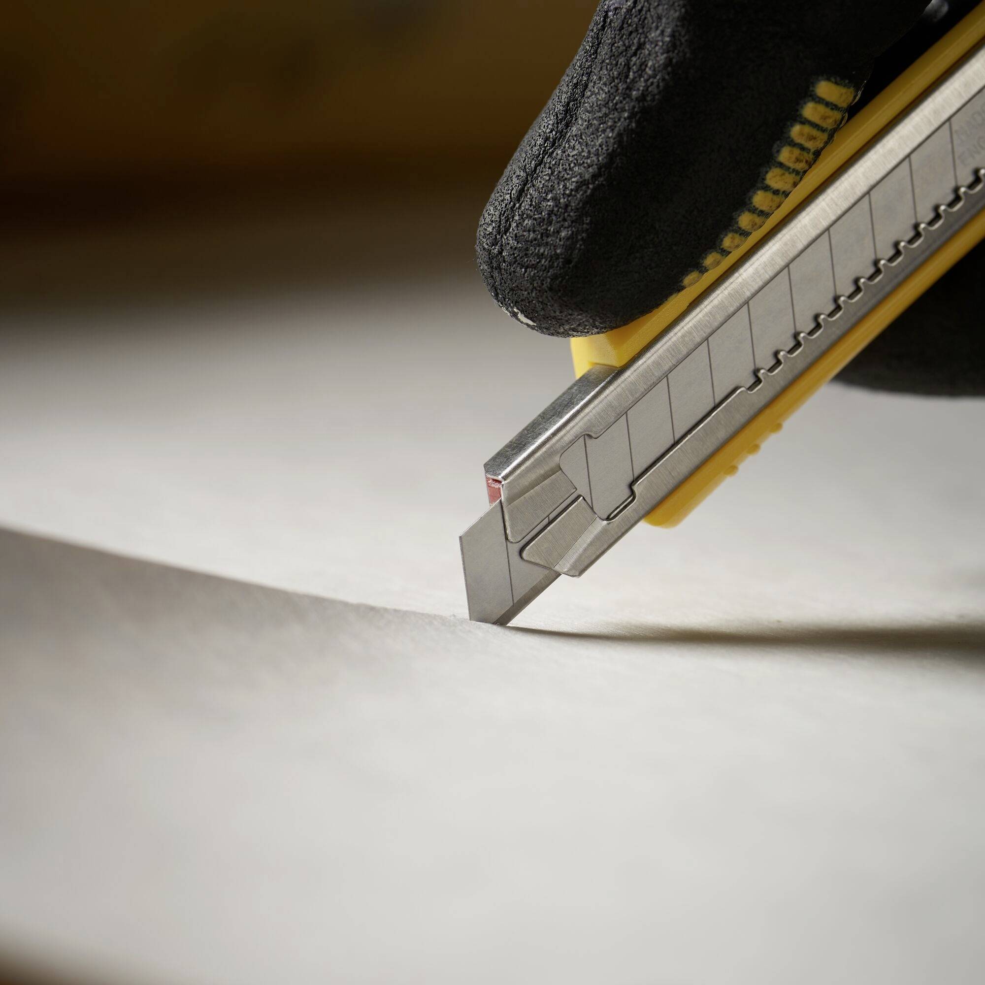 Ein Cuttermesser in einem schwarzen Handschuh schneidet ein Blatt Papier auf einem Tisch.