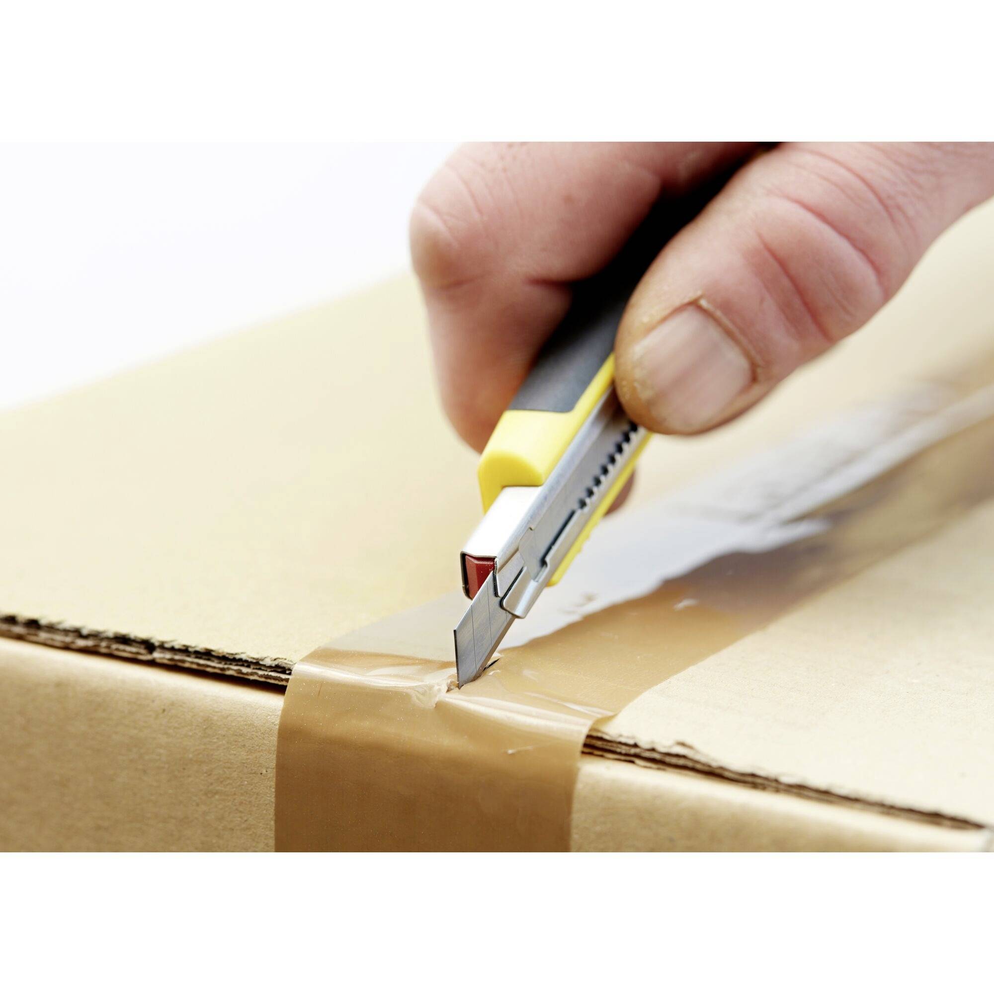 Eine Hand öffnet vorsichtig einen mit Klebeband versiegelten Karton mit einem gelben Cutter-Messer.