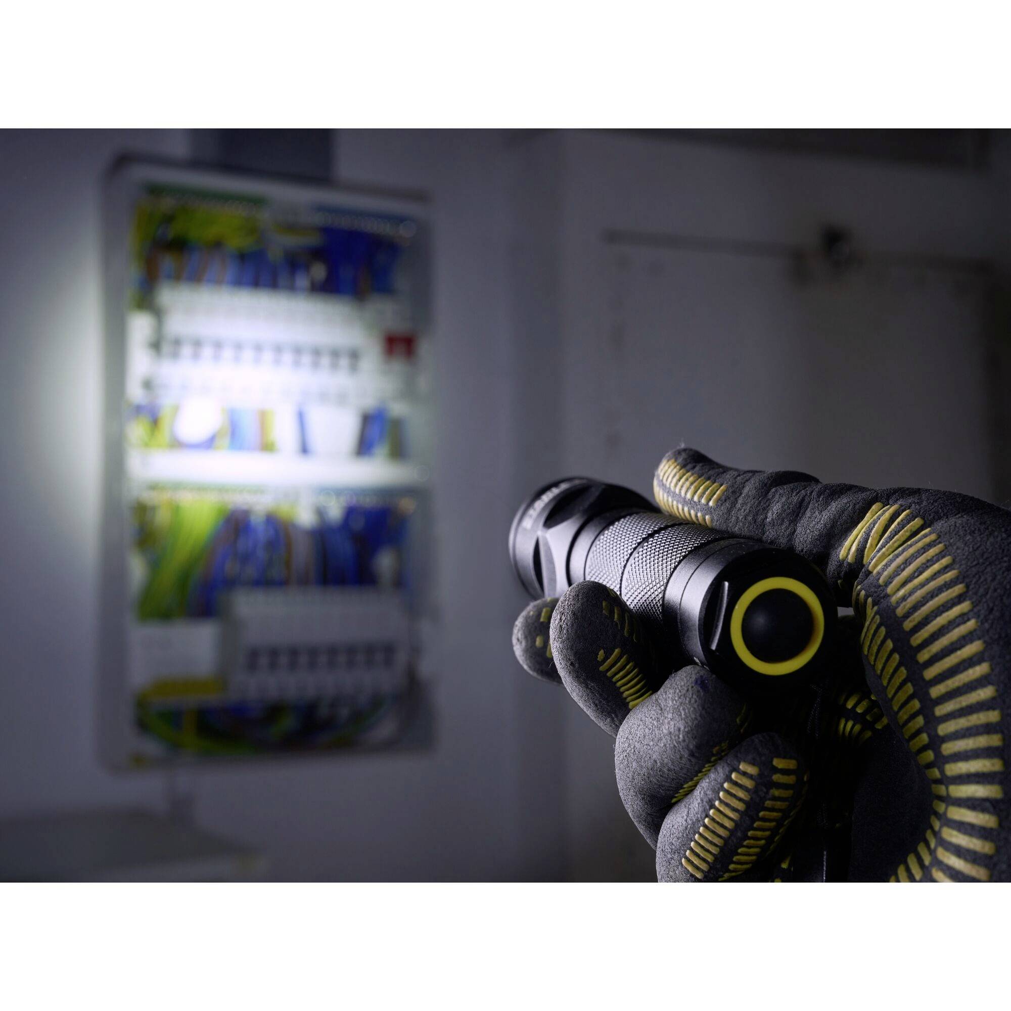 Eine Hand in Arbeitshandschuh hält eine Taschenlampe, die auf einen geöffneten Elektrokasten leuchtet, um Kabel und Komponenten zu beleuchten.