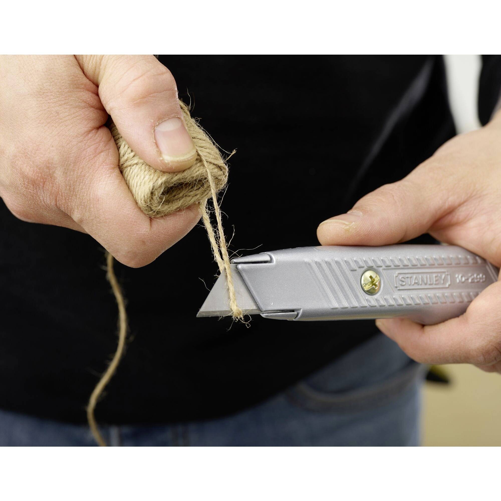 Person hält ein Cutter-Messer und schneidet ein Seil.