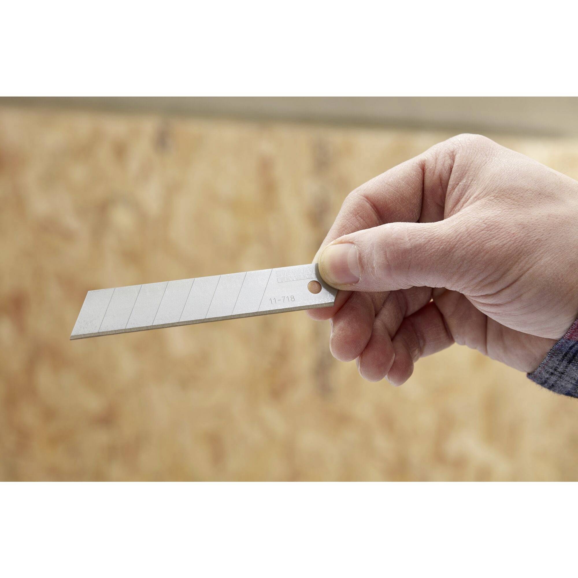 Eine Hand hält ein silbernes Abbrechklingenmesser vor einem unscharfen Hintergrund aus Holzstruktur.