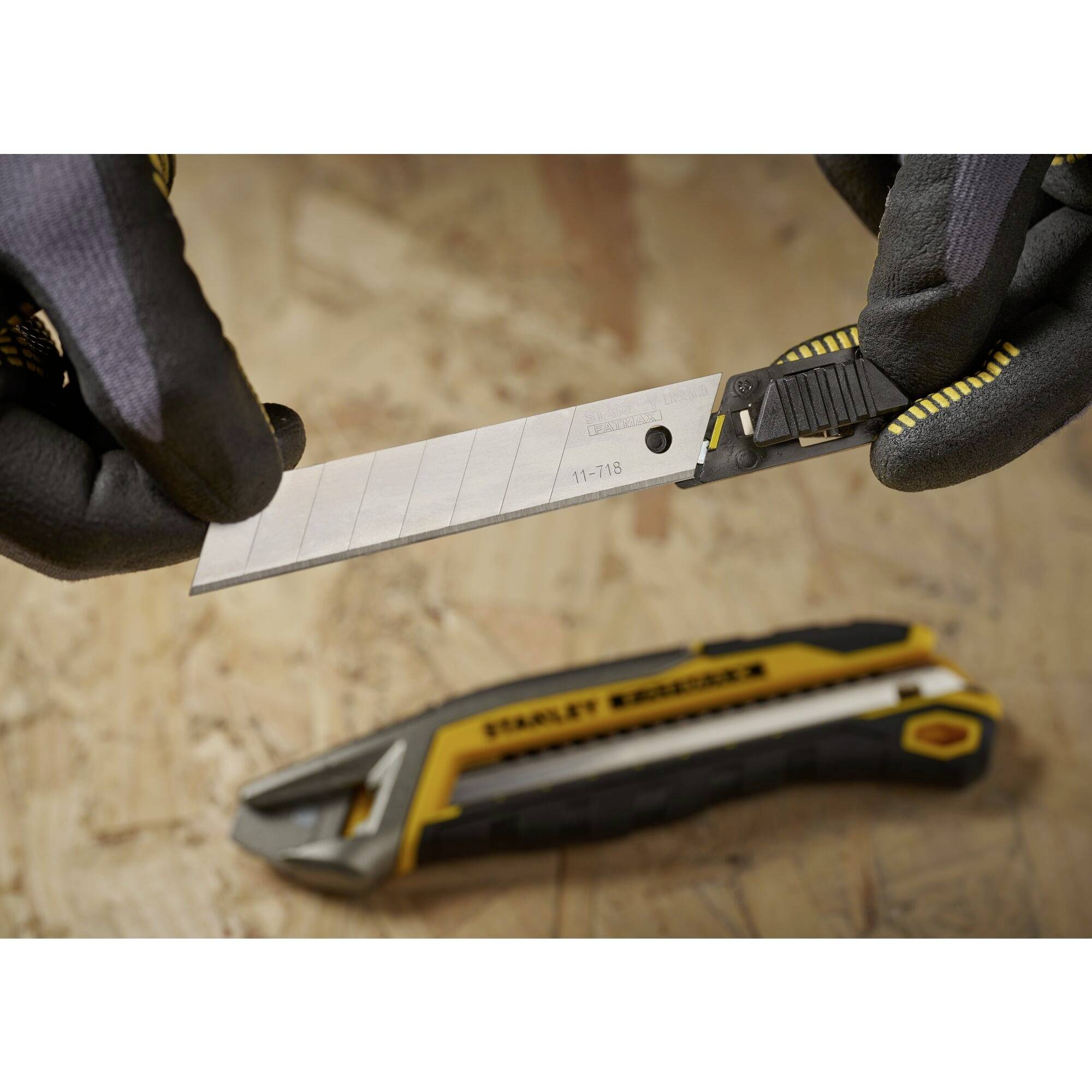 Eine Person hält ein Cuttermesser, während ein weiteres Cuttermesser auf einem Holztisch liegt. Beide Messer sind schwarz-gelb.