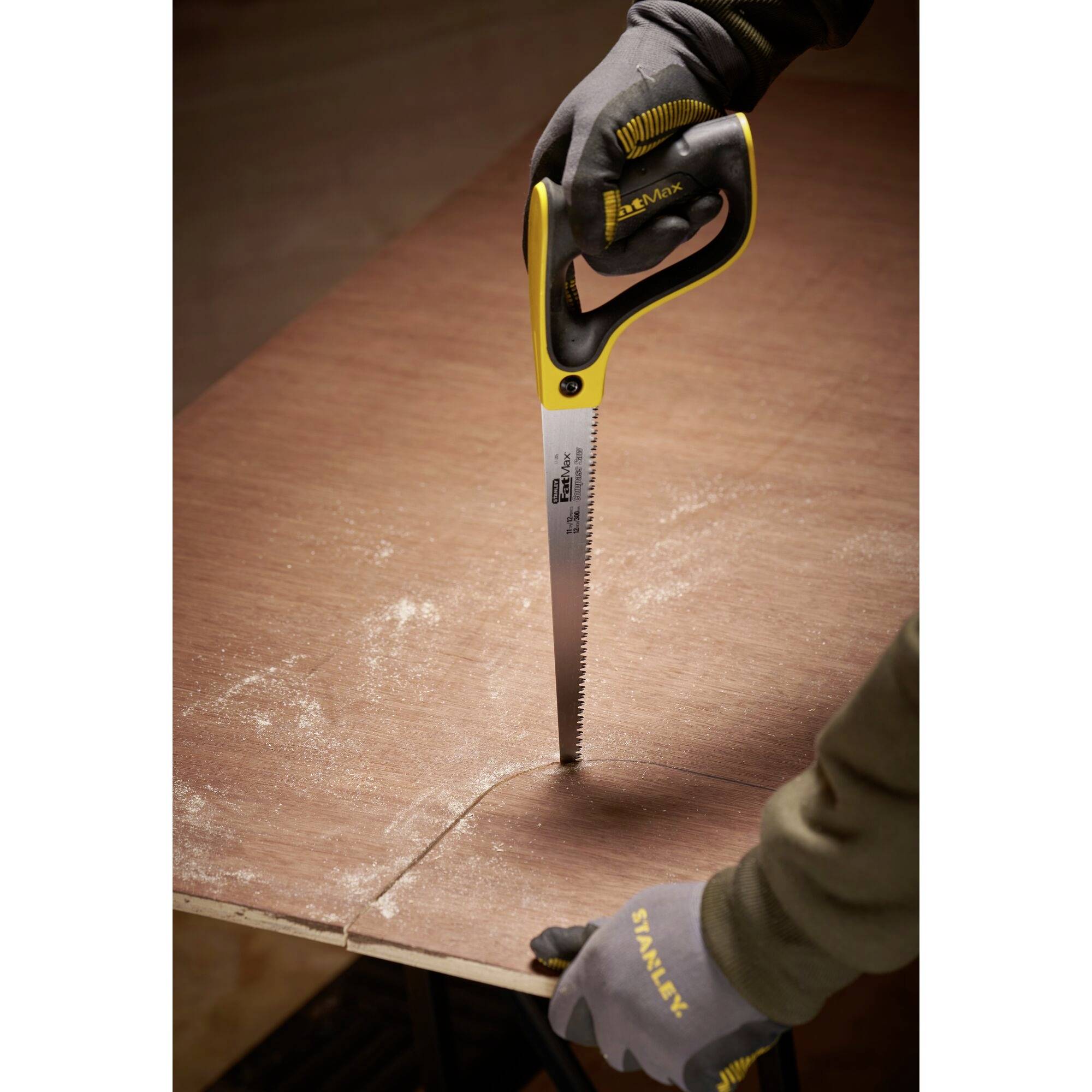 Eine Person schneidet mit einer Handsäge präzise eine Holzplatte entlang einer markierten Linie. Sie trägt Handschuhe.