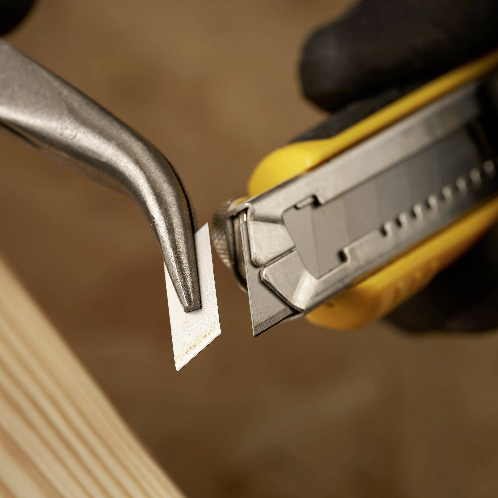 Nahaufnahme eines Cuttermessers mit herausgeschobener Klinge, die ein Stück Papier schneidet. Fokus auf die Klinge und die Holzoberfläche darunter.