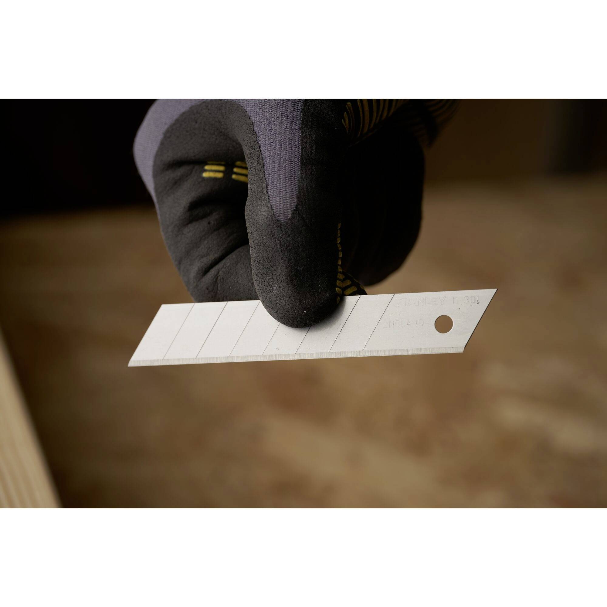 Eine Hand in einem Arbeitshandschuh hält eine Klinge mit glatter Oberfläche und Loch an einem Ende. Hintergrund unscharf.