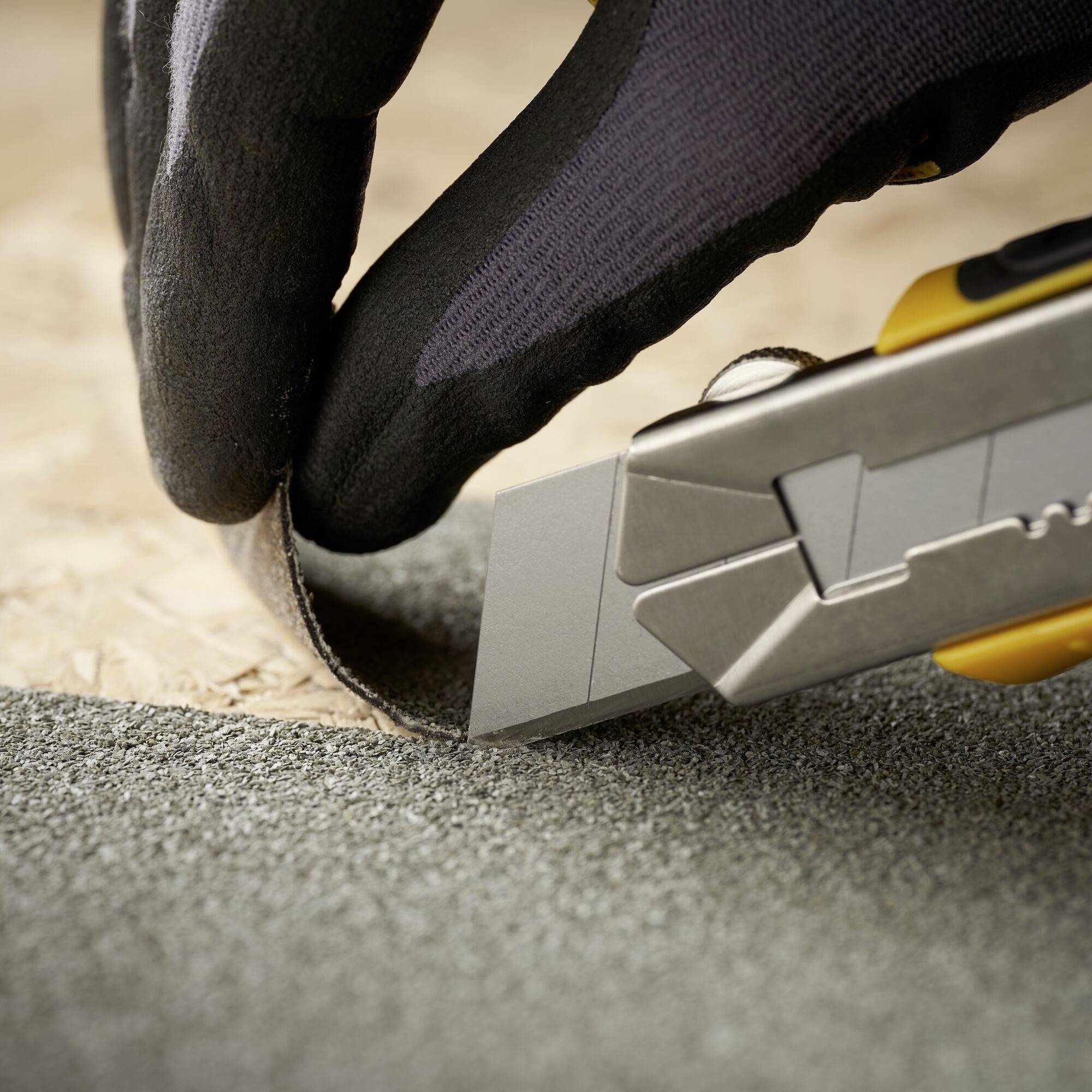 Eine Person schneidet mit einem Cuttermesser über Sandpapier. Fokus liegt auf dem Messer und der präzisen Schneidearbeit.