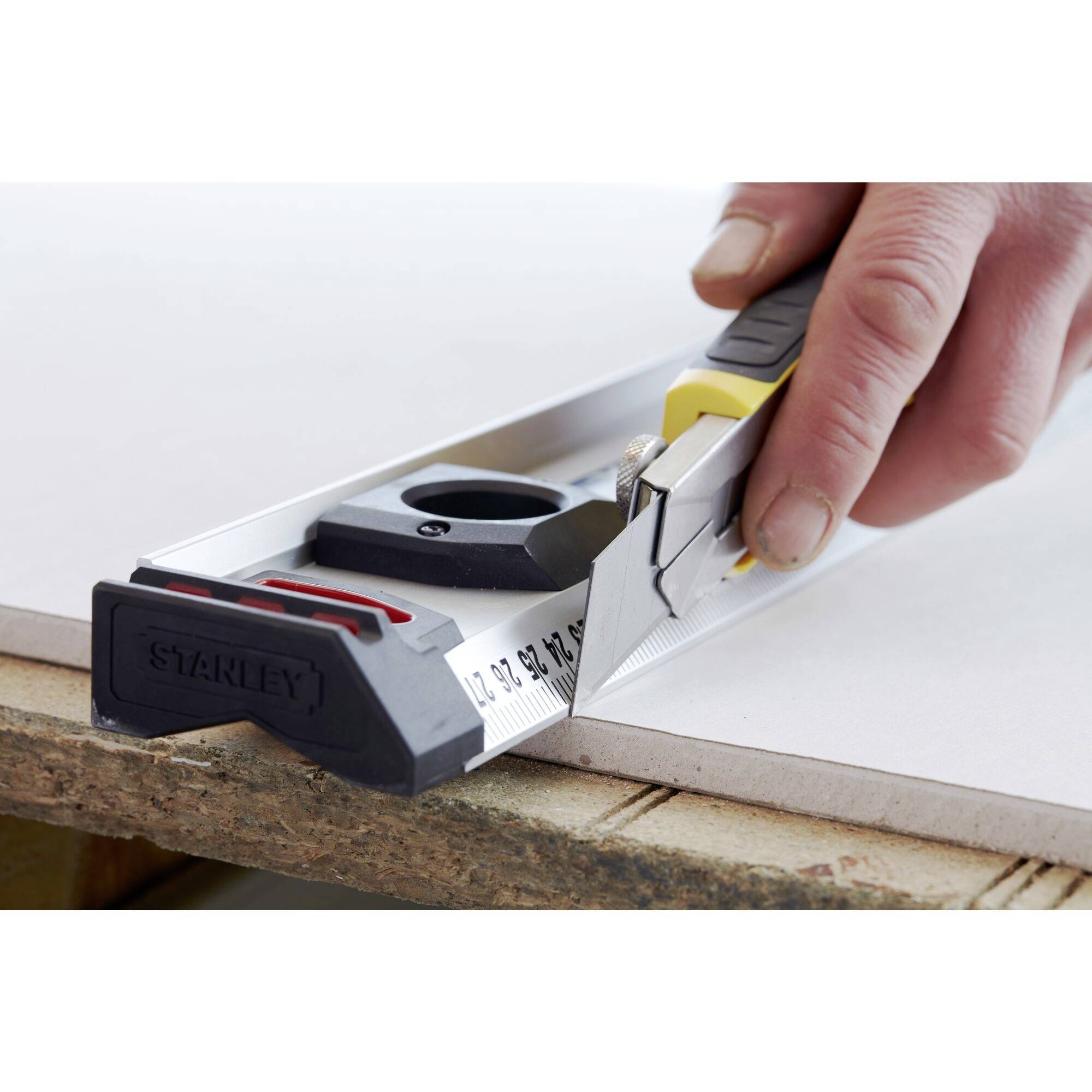 Eine Hand zieht mit einem Cuttermesser entlang eines Lineals auf einer Holzplatte, um einen geraden Schnitt zu machen.