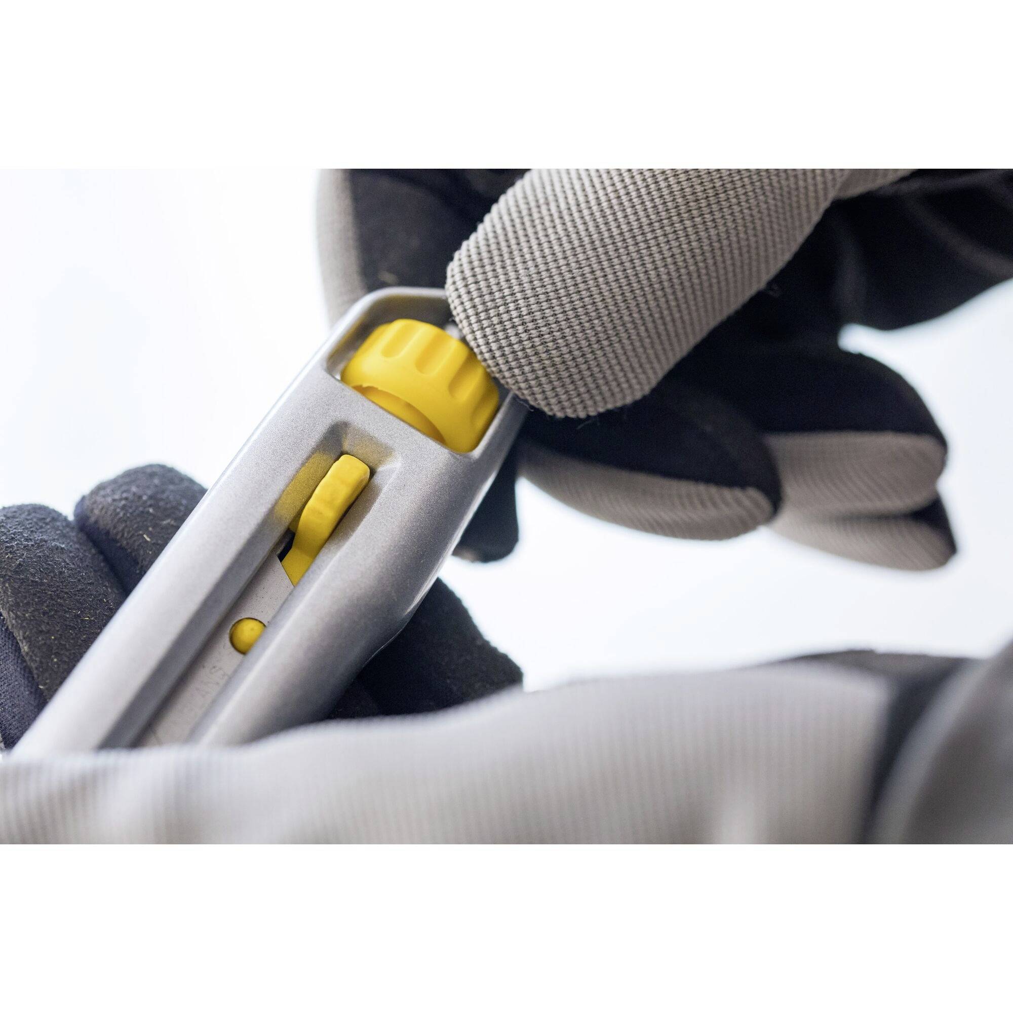 Eine Person mit Handschuhen hält einen silbernen Cutter mit einem gelben Schiebemechanismus, bereit zum Schneiden.