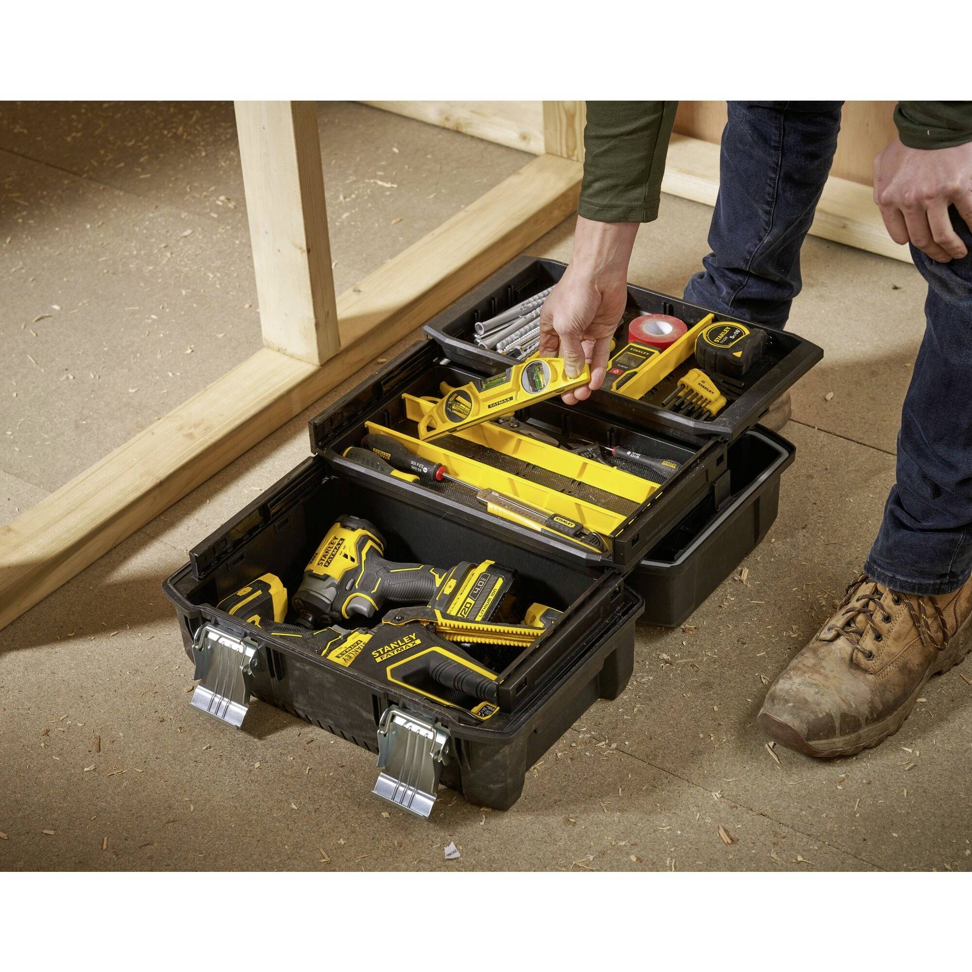 Ein geöffneter Werkzeugkasten auf einem Holzboden, gefüllt mit Schraubendreher, Maßband, Bohrmaschine und weiteren Werkzeugen.