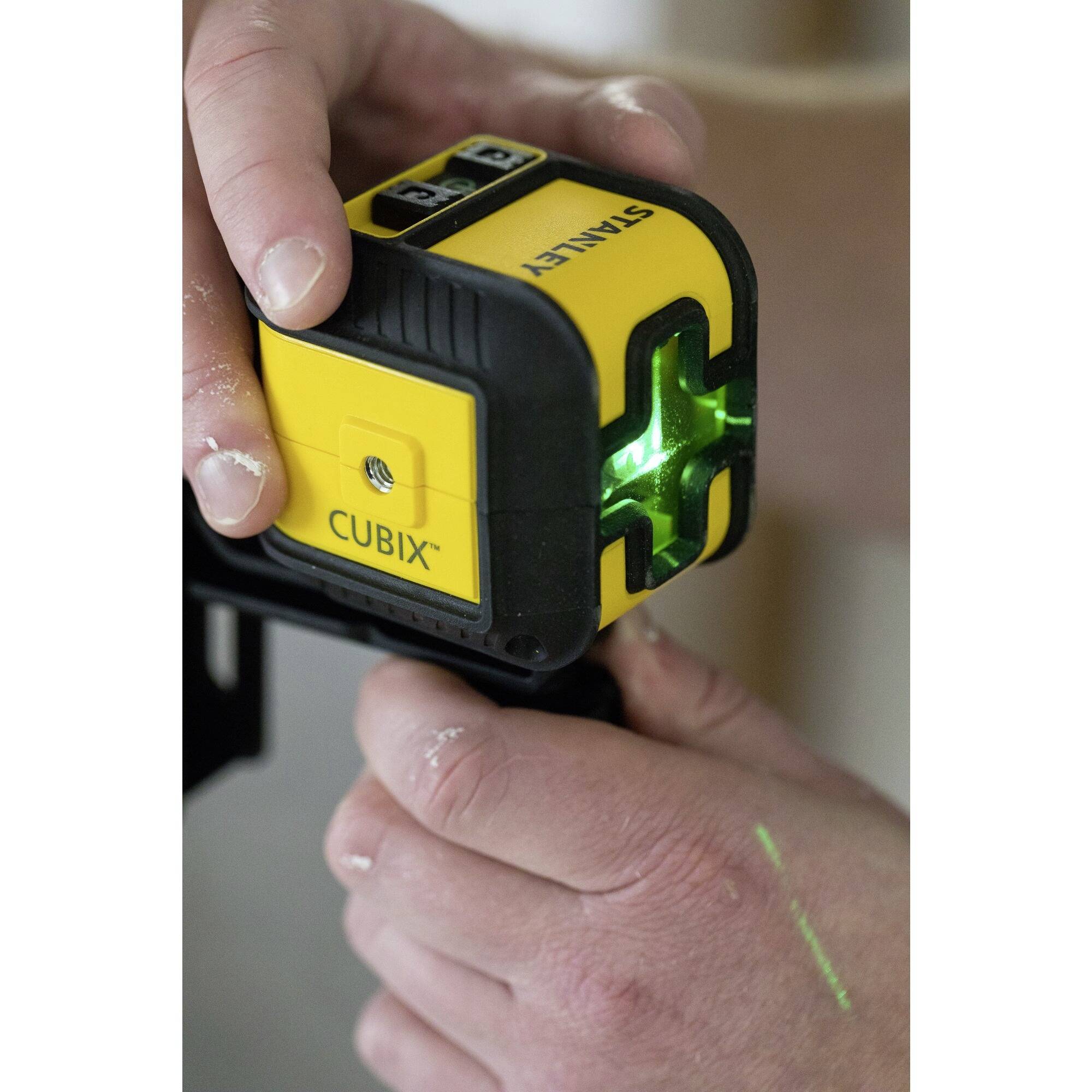 Eine Person hält einen gelben Laser mit grüner Lichtprojektion, vermutlich zur genauen Vermessung oder Ausrichtung von Objekten.