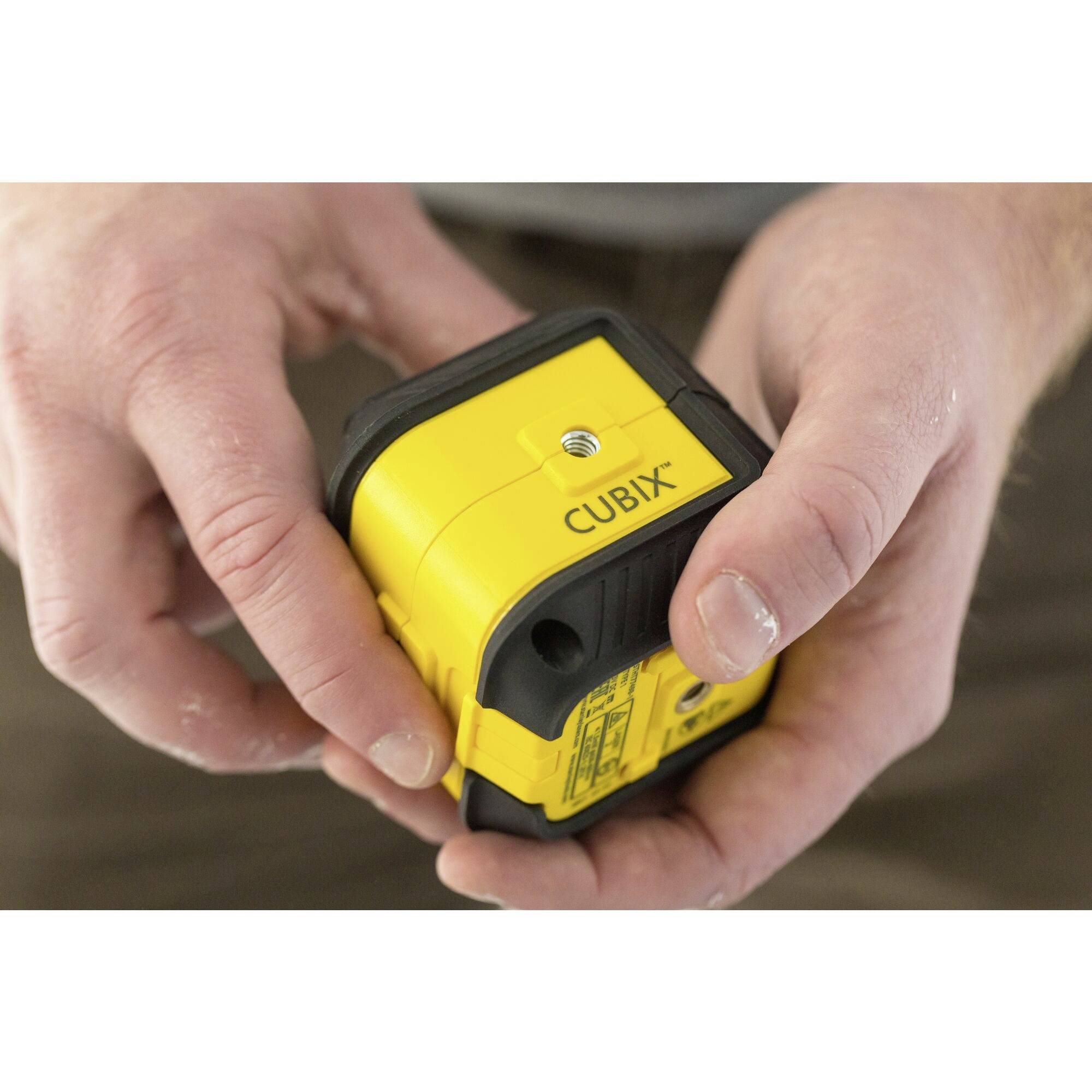 Person hält einen gelben Laser-Entfernungsmesser mit der Aufschrift 'CUBIX' in den Händen.
