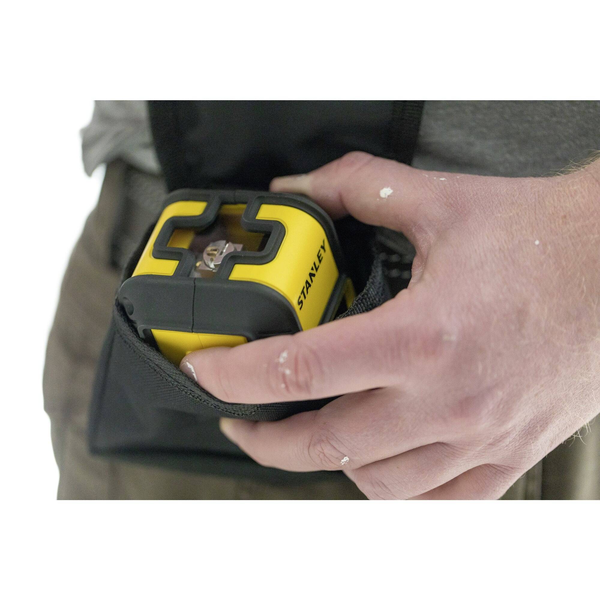 Eine Person hält ein gelbes Lasermessgerät in einer Tasche. Das Gerät zeigt digital gemessene Werte an, die für Bauarbeiten nützlich sind.