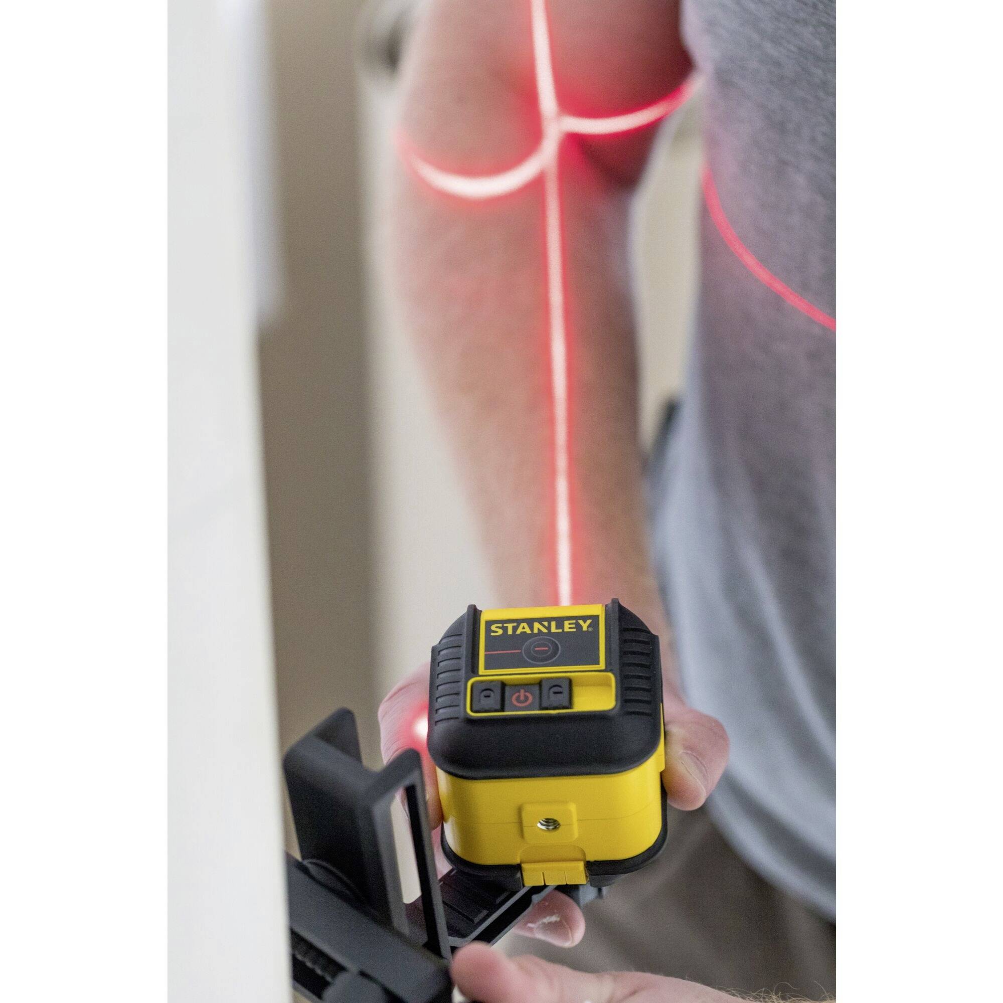 Eine Person verwendet ein Laser-Nivelliergerät an der Wand. Rote Laserlinien zeigen vertikal und horizontal die Nivellierungen an.