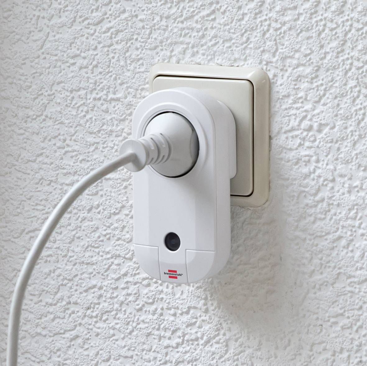 Eine Steckdose mit einem eingesteckten Stecker und einem Überspannungsschutz an einer weißen Wand.