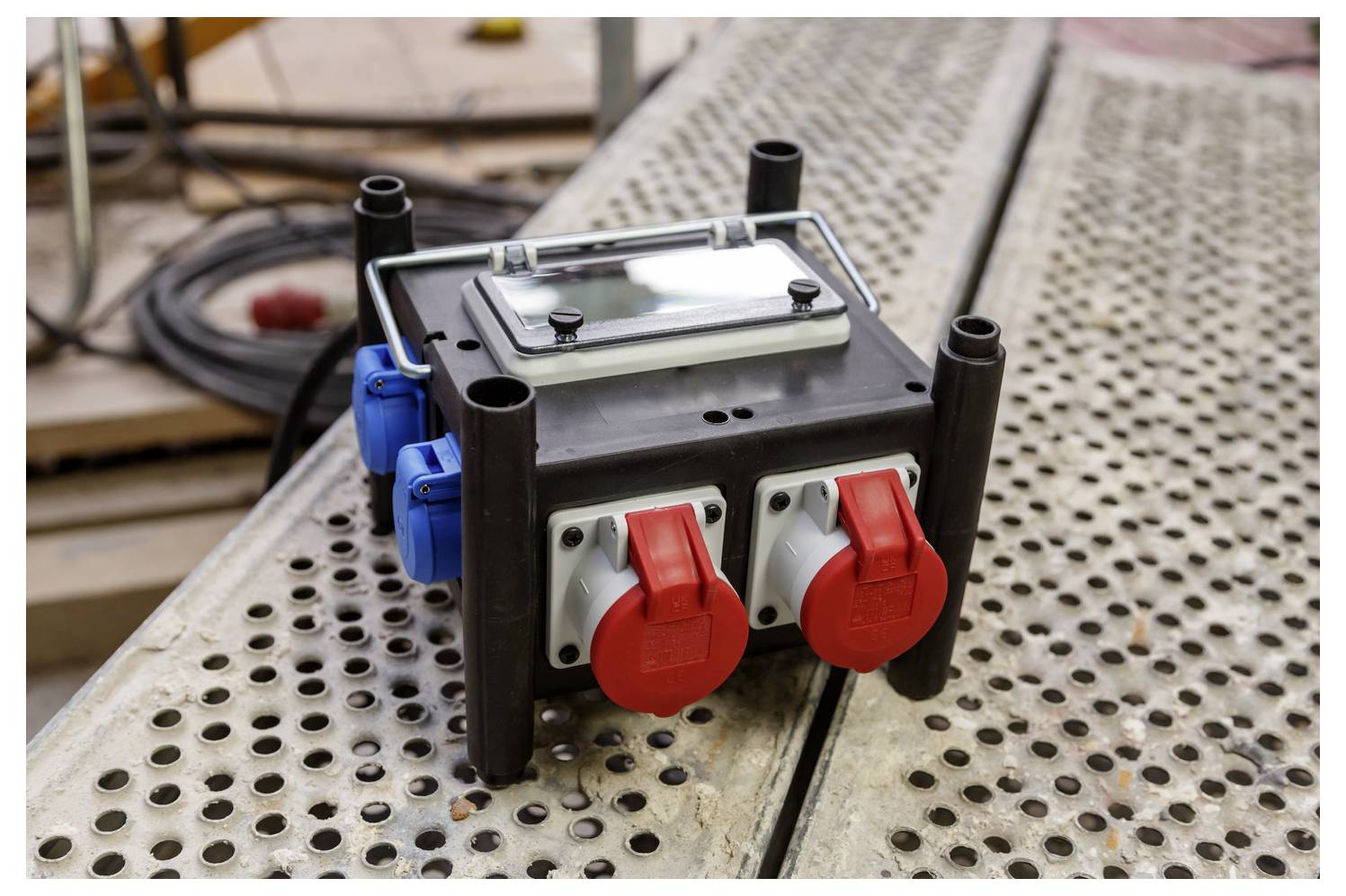 Tragbare Stromverteilungsbox mit roten und blauen Steckdosen auf einer perforierten Metallfläche zur Arbeit.