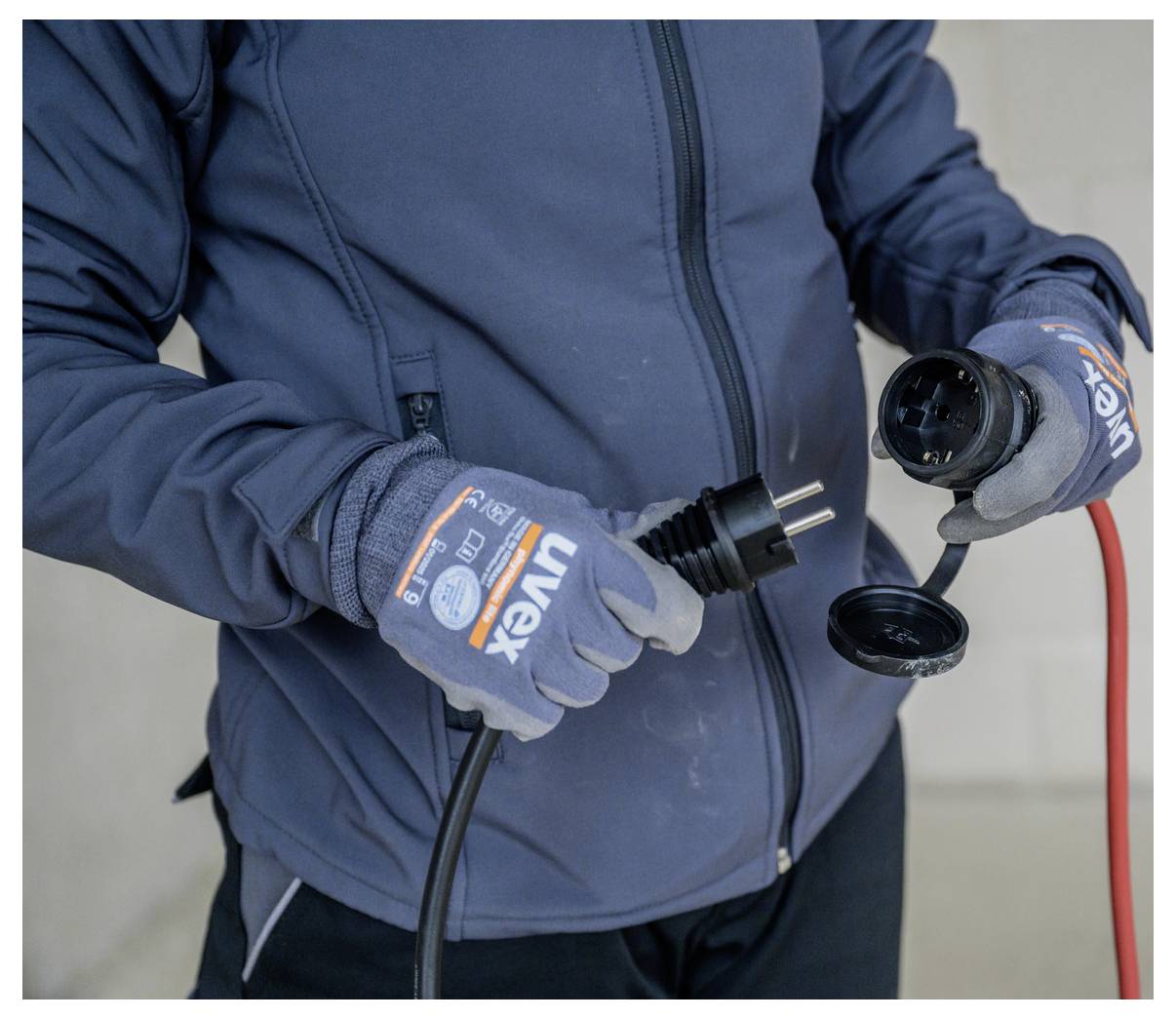 Person in Handschuhen hält einen Stromstecker und eine passende Steckdose mit Schutzkappe und bereitet sich darauf vor, ein Verlängerungskabel oder ein Außenelektrokabel anzuschließen.